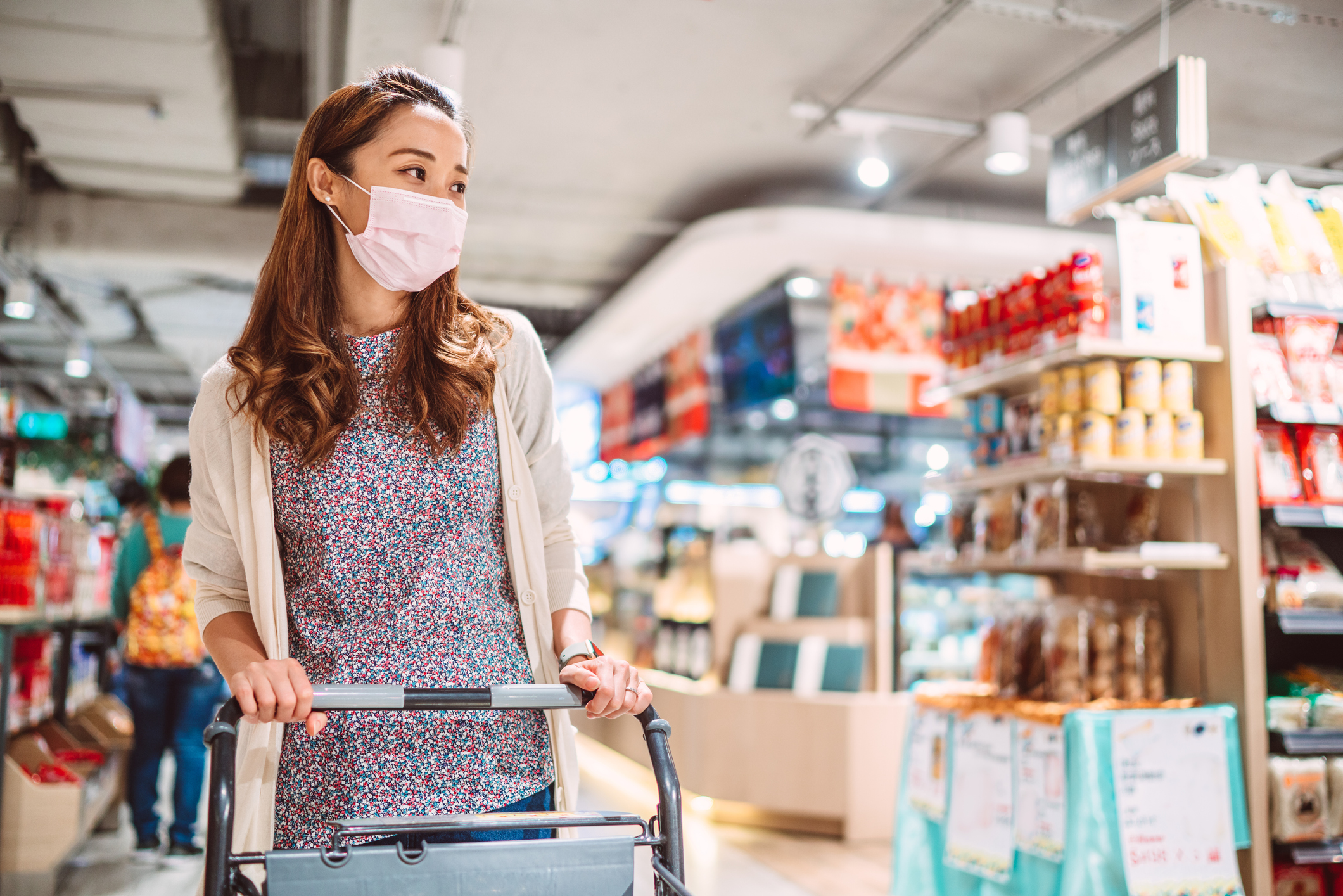 A woman wearing a mask and pushing a shopping trolley in a store.