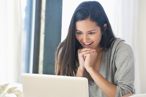 A smiling person looking at a laptop.