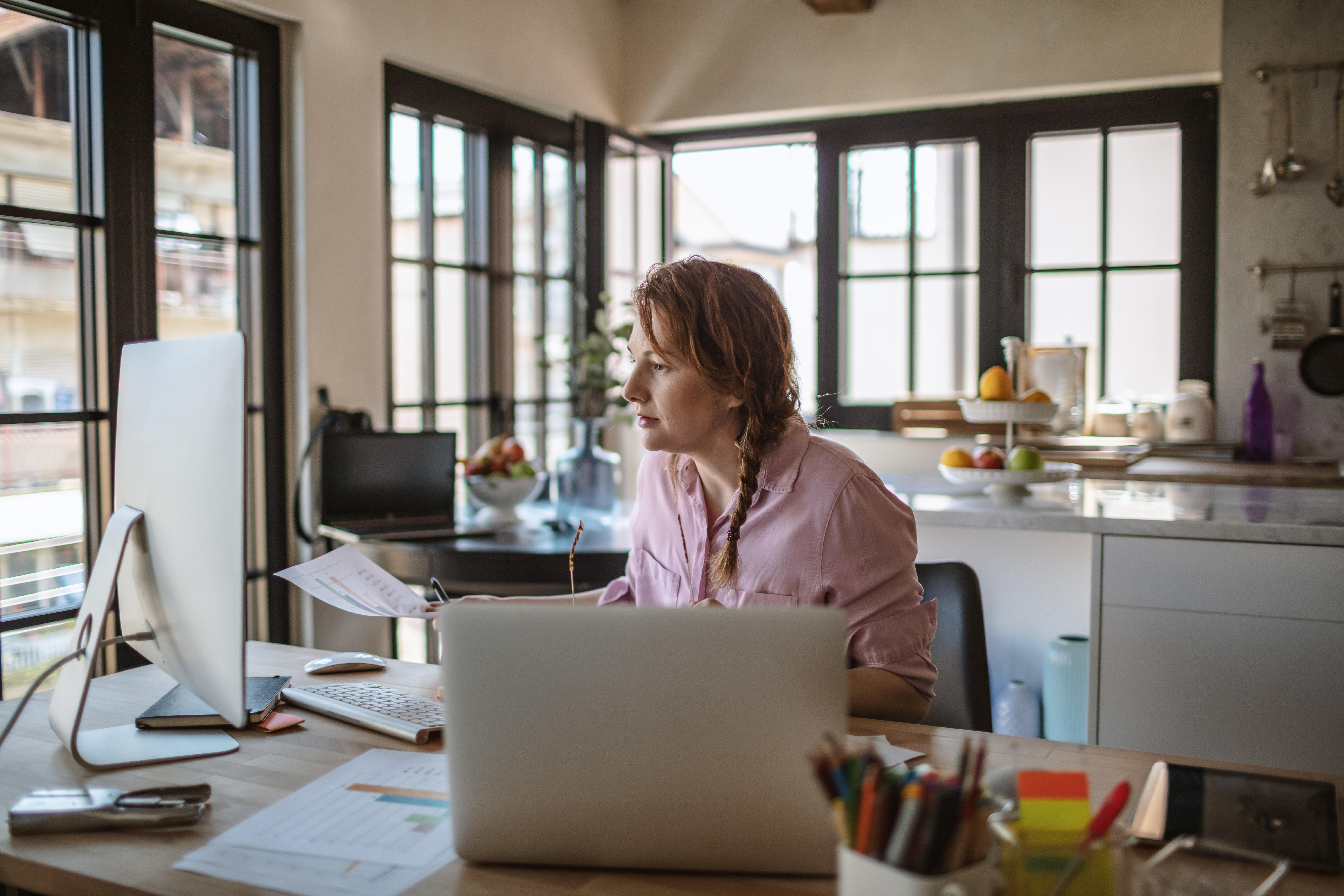 Adult sits at a desk at home in front of a laptop and monitor.