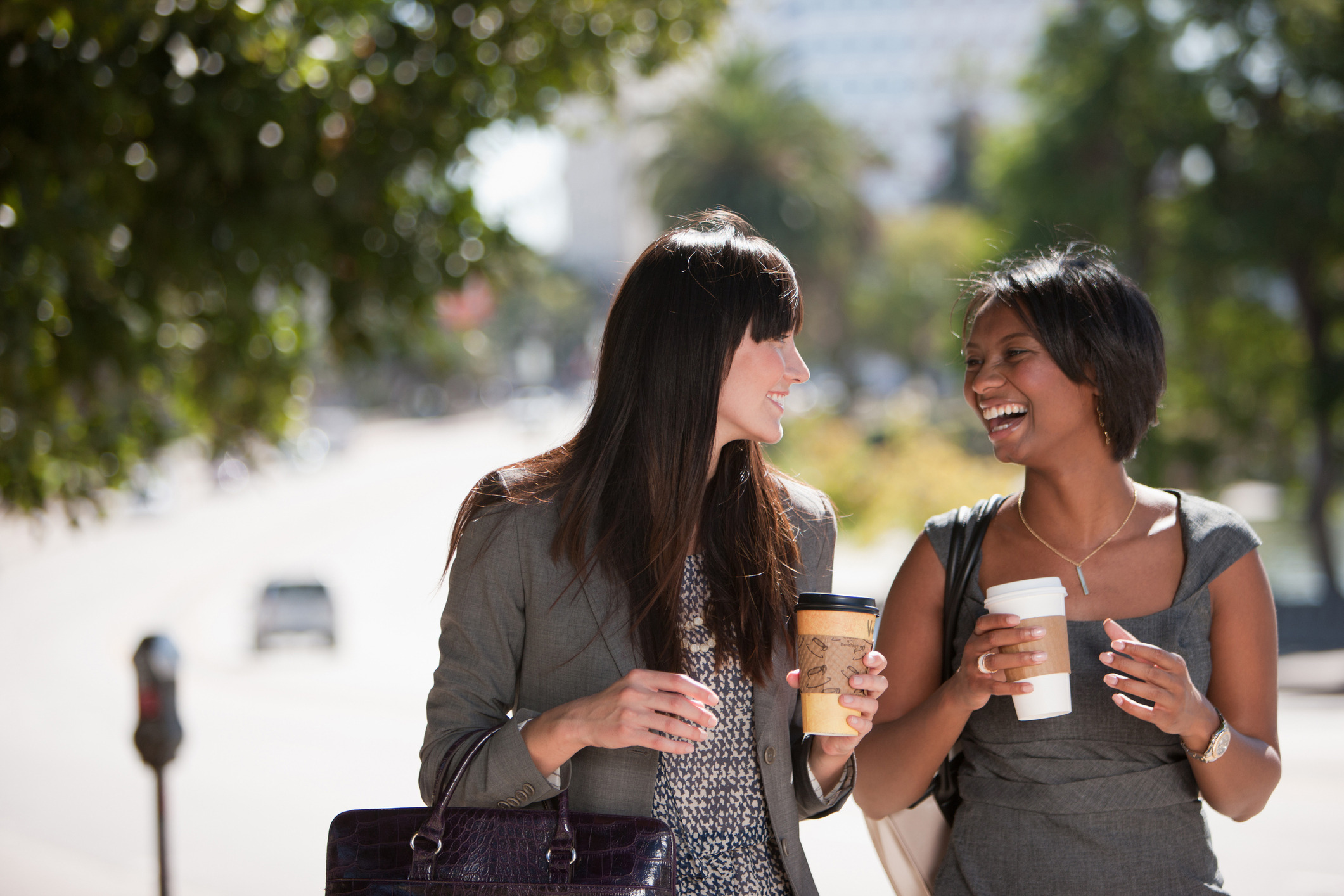 Two people walking together and holding paper cups of coffee.
