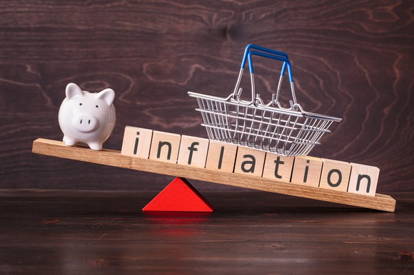 A lever balancing blocks that spell out inflation with a piggy bank