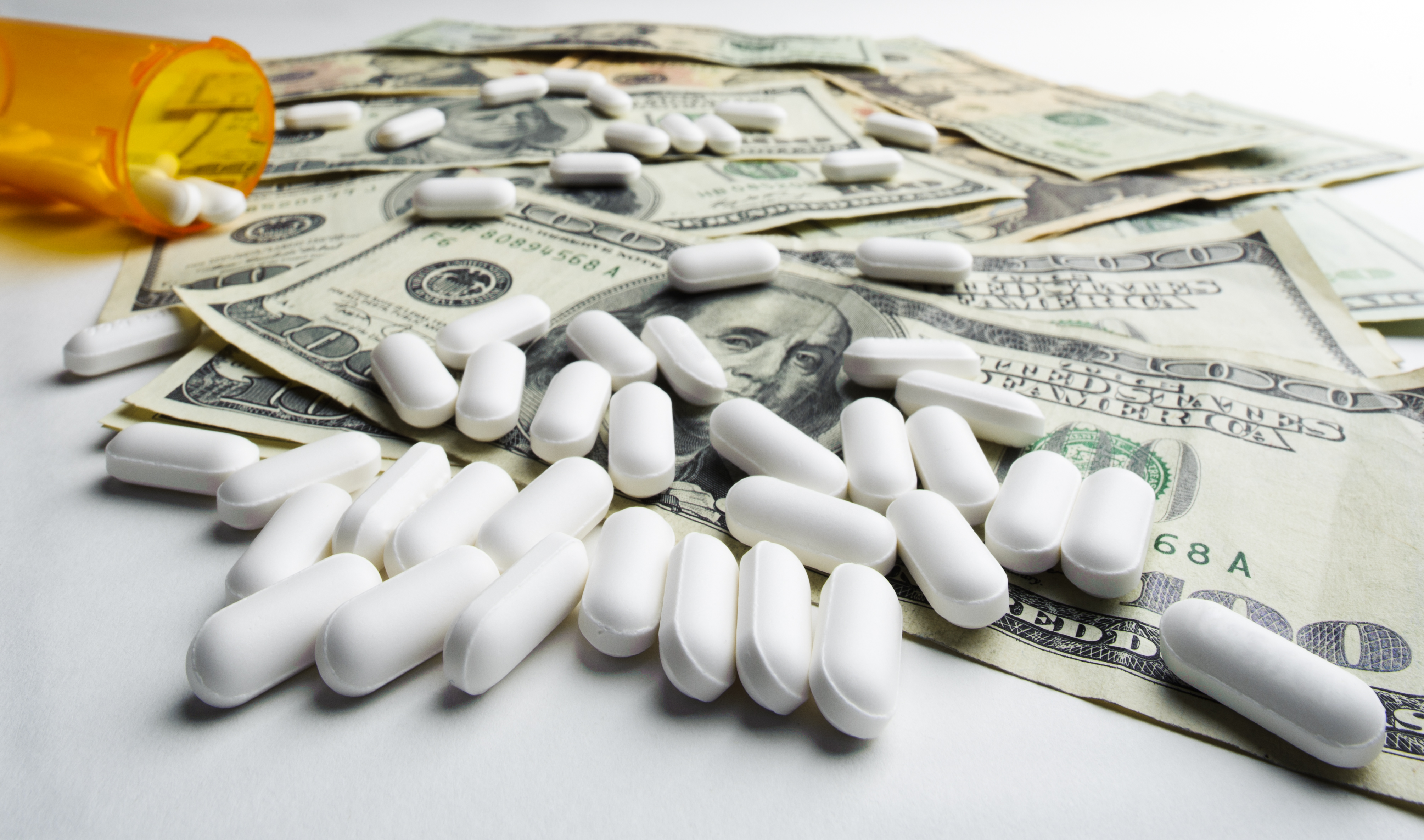 Prescription bottle spilling pills onto $100 bills.