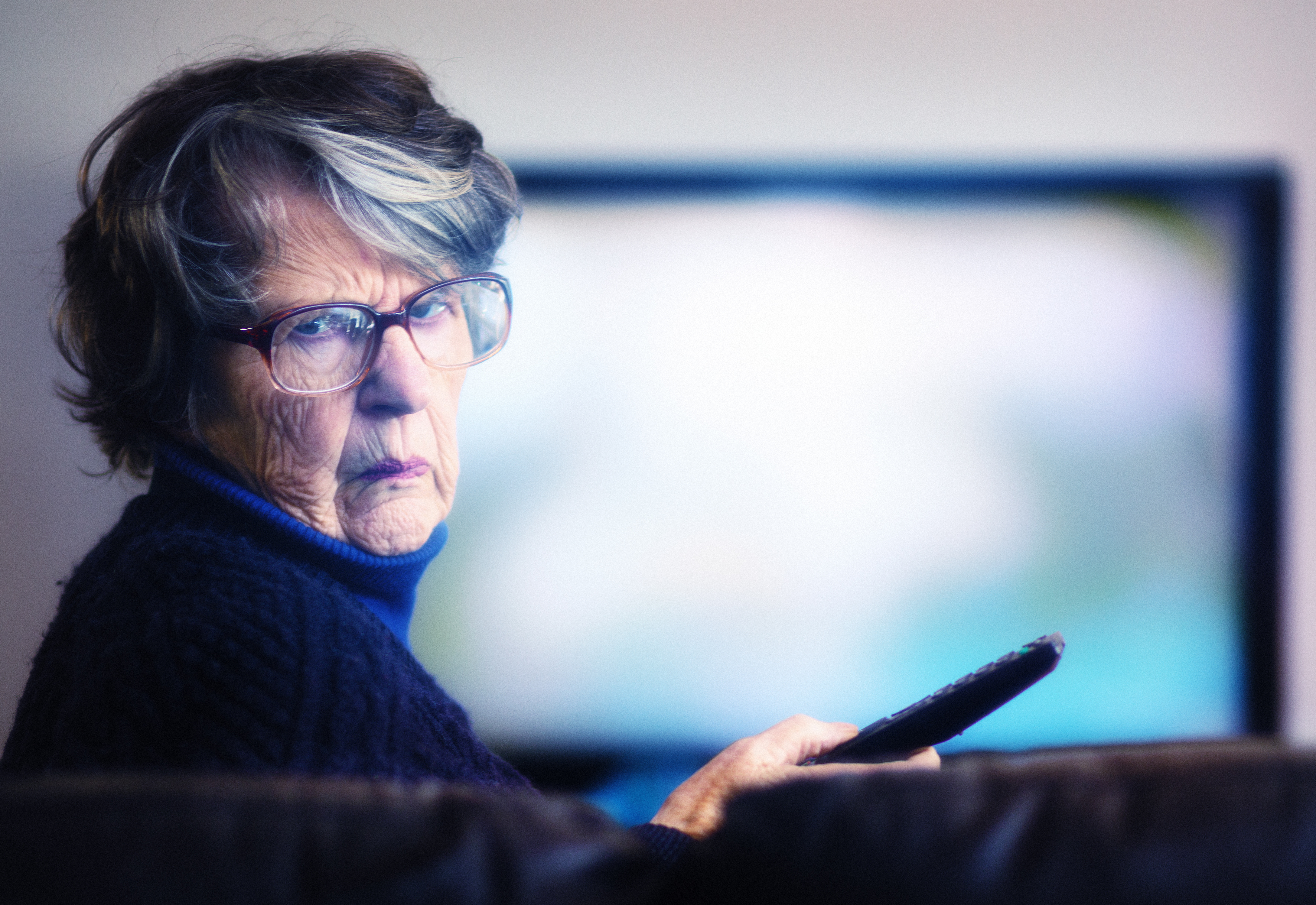 Person looking disappointed holding a remote in front of a blurry TV.
