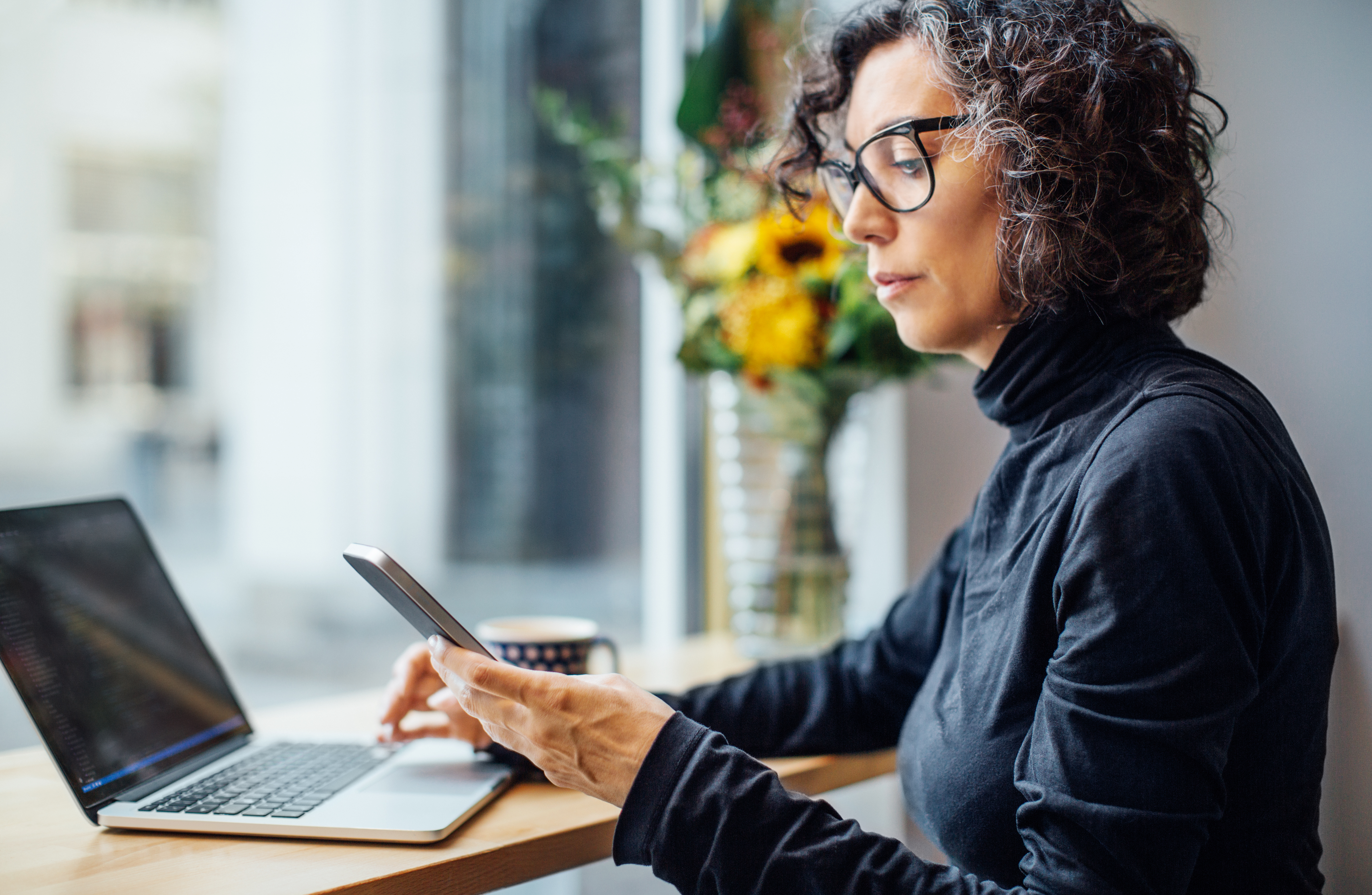 A person using a notebook computer and smartphone with a neutral look on their face.