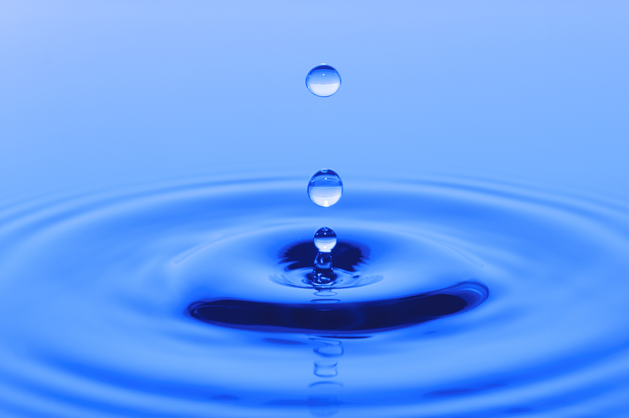 Drops of water falling into a deep blue body of water and causing ripples.