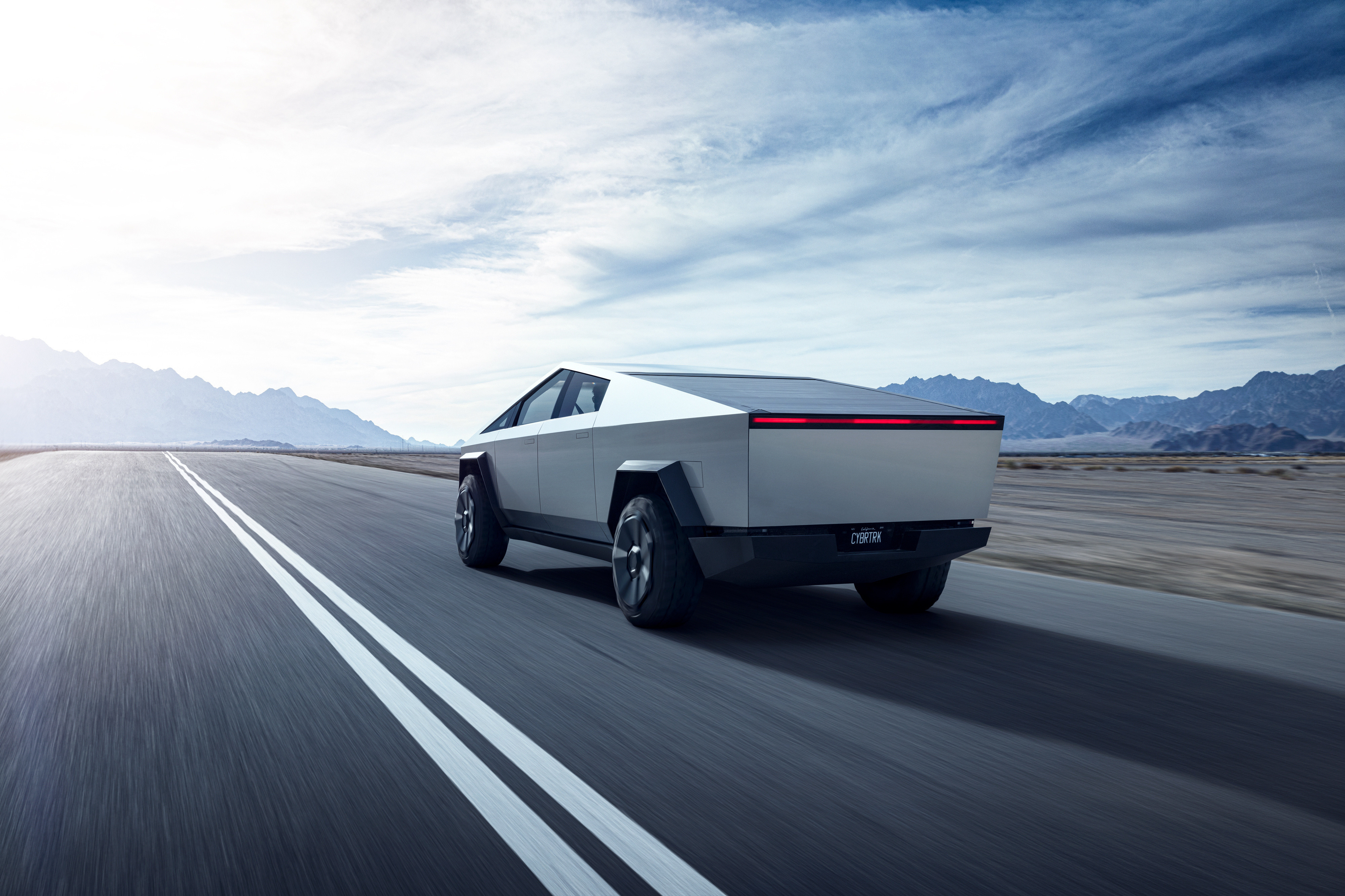 The Tesla Cybertruck speeding along a highway toward sunrise over the mountains.