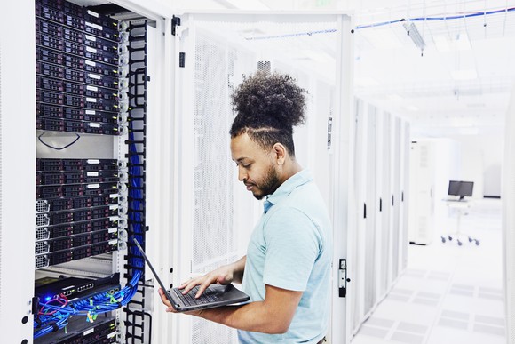An IT professional analyzing a laptop while plugged into a server.