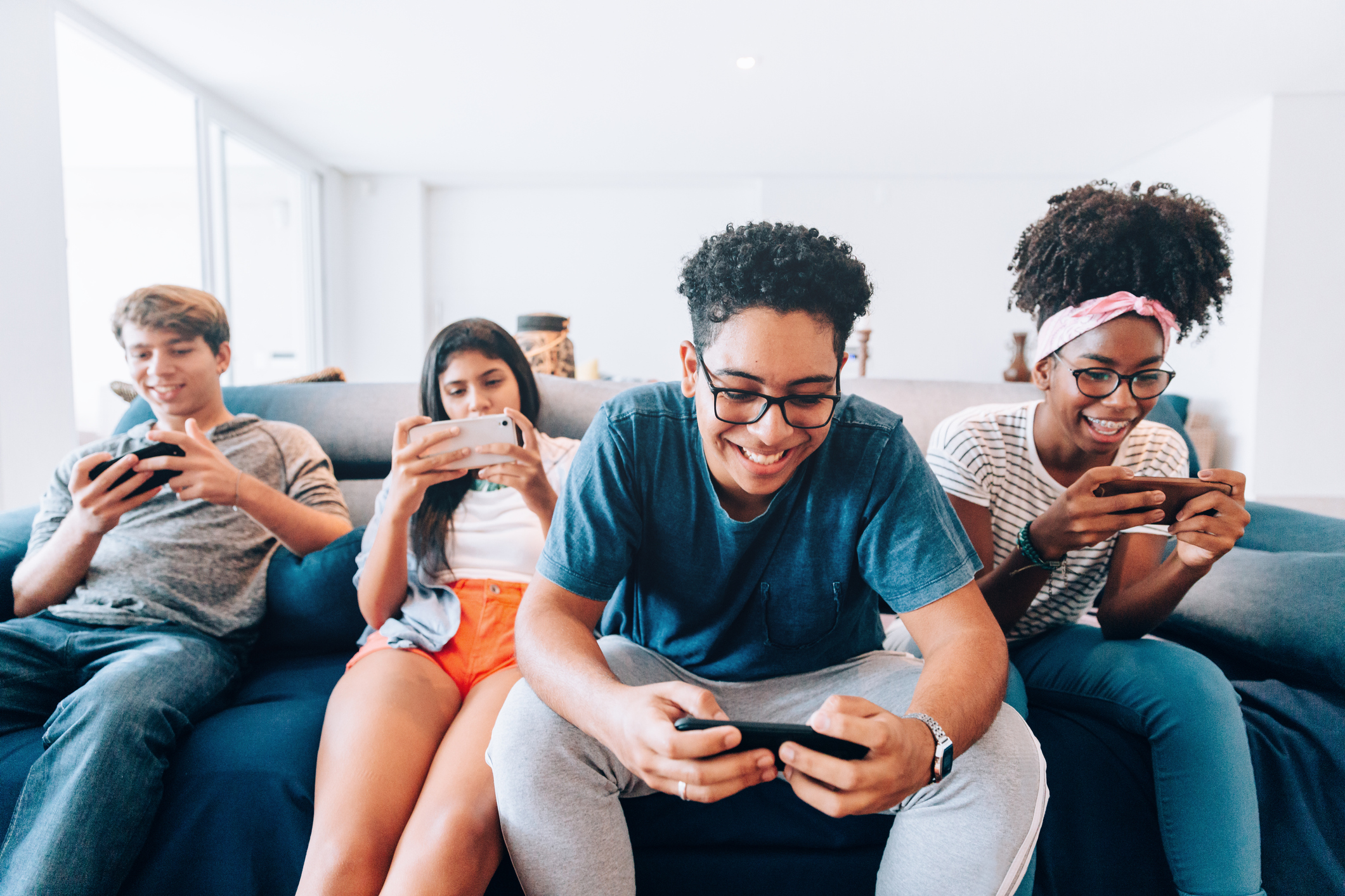 Teens playing video games on their phones while sitting on a couch.