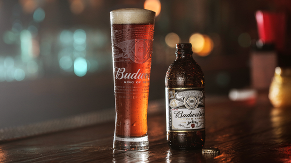 A glass and bottle of Budweiser next to each other on a bar.