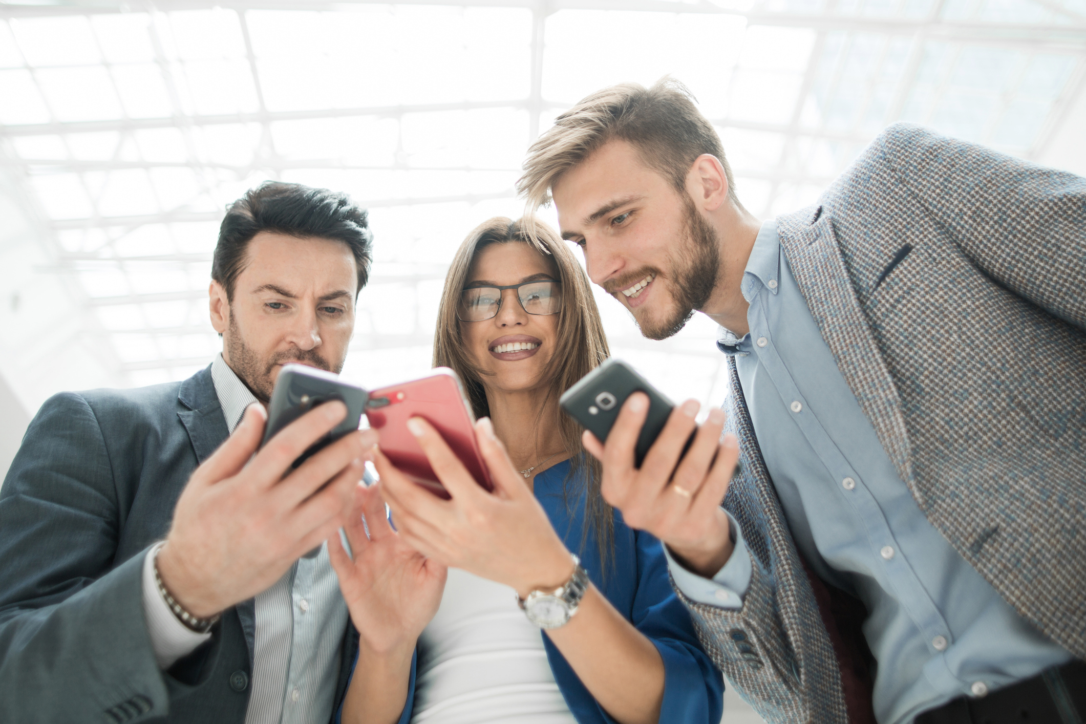 Three people gathered together looking at their smartphones.