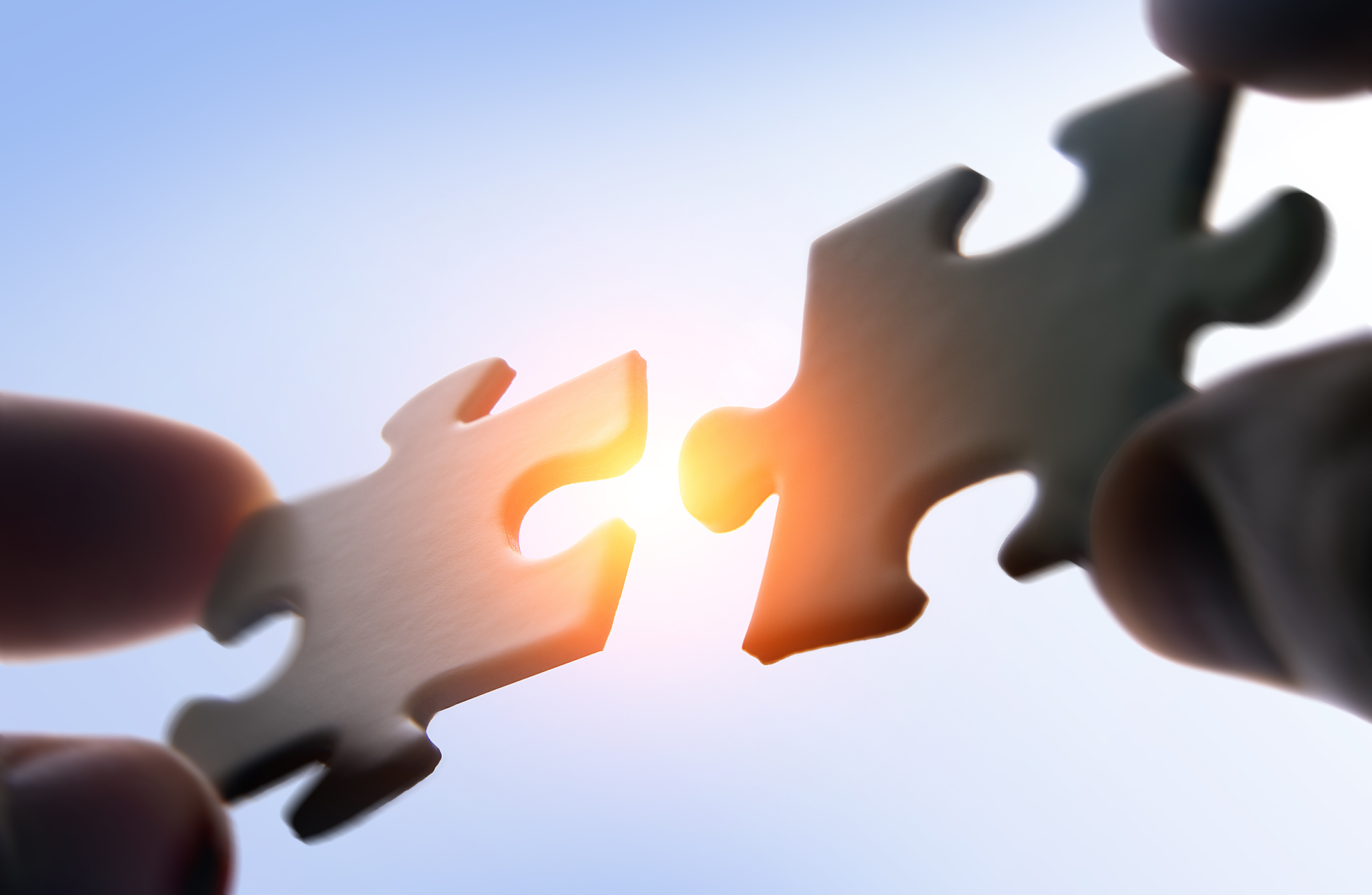 A person putting two puzzle pieces together with sunlight in the background.