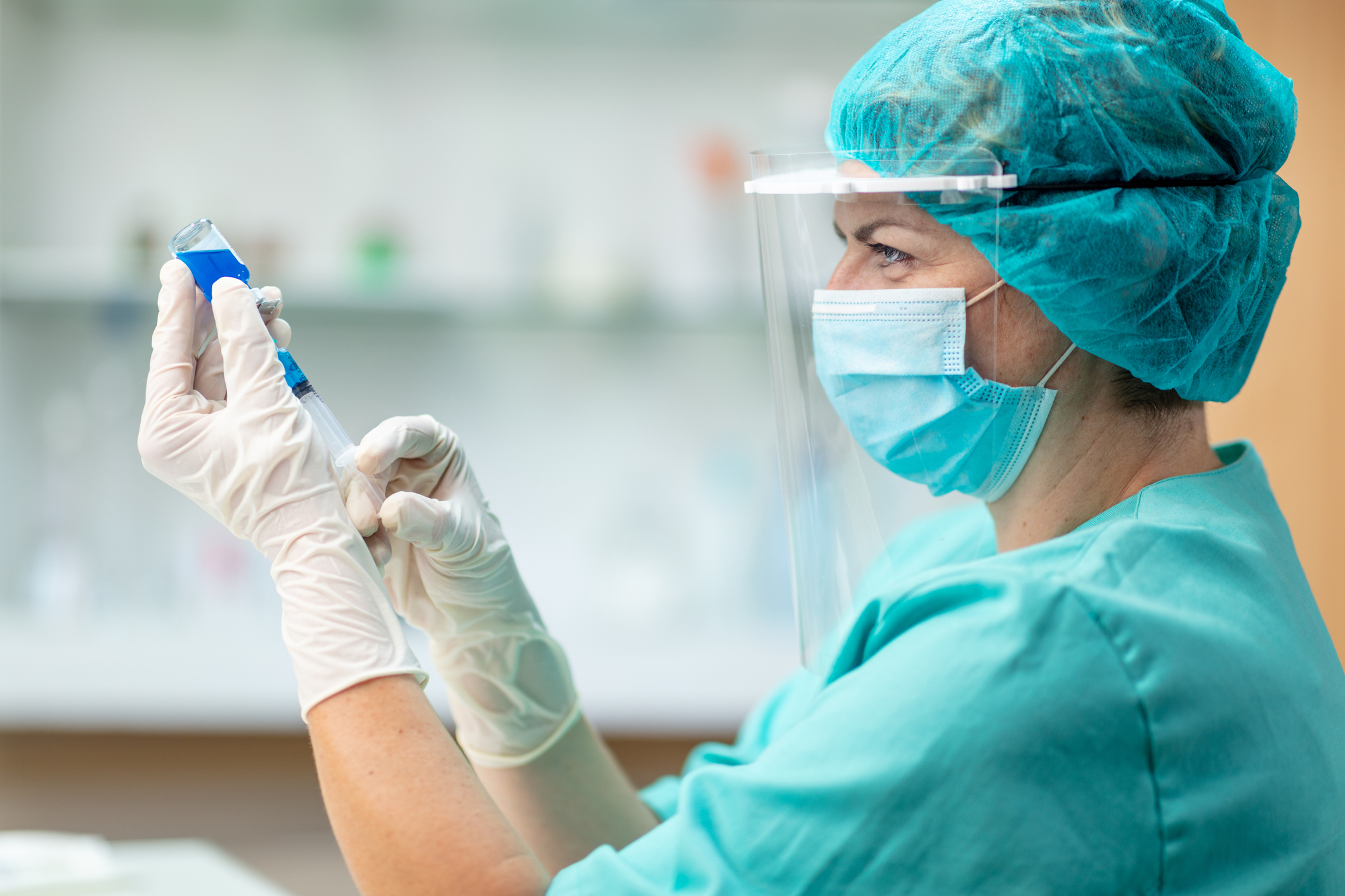 A nurse wearing full protective equipment loads a syringe from a vial of coronavirus vaccine.