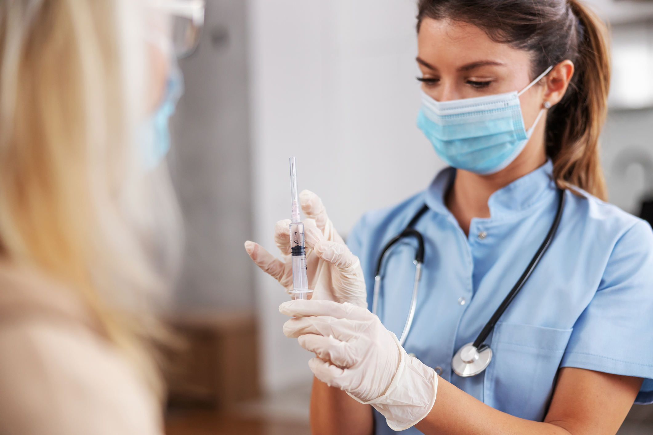 A masked and gloved healthcare worker prepares a syringe for vaccination.