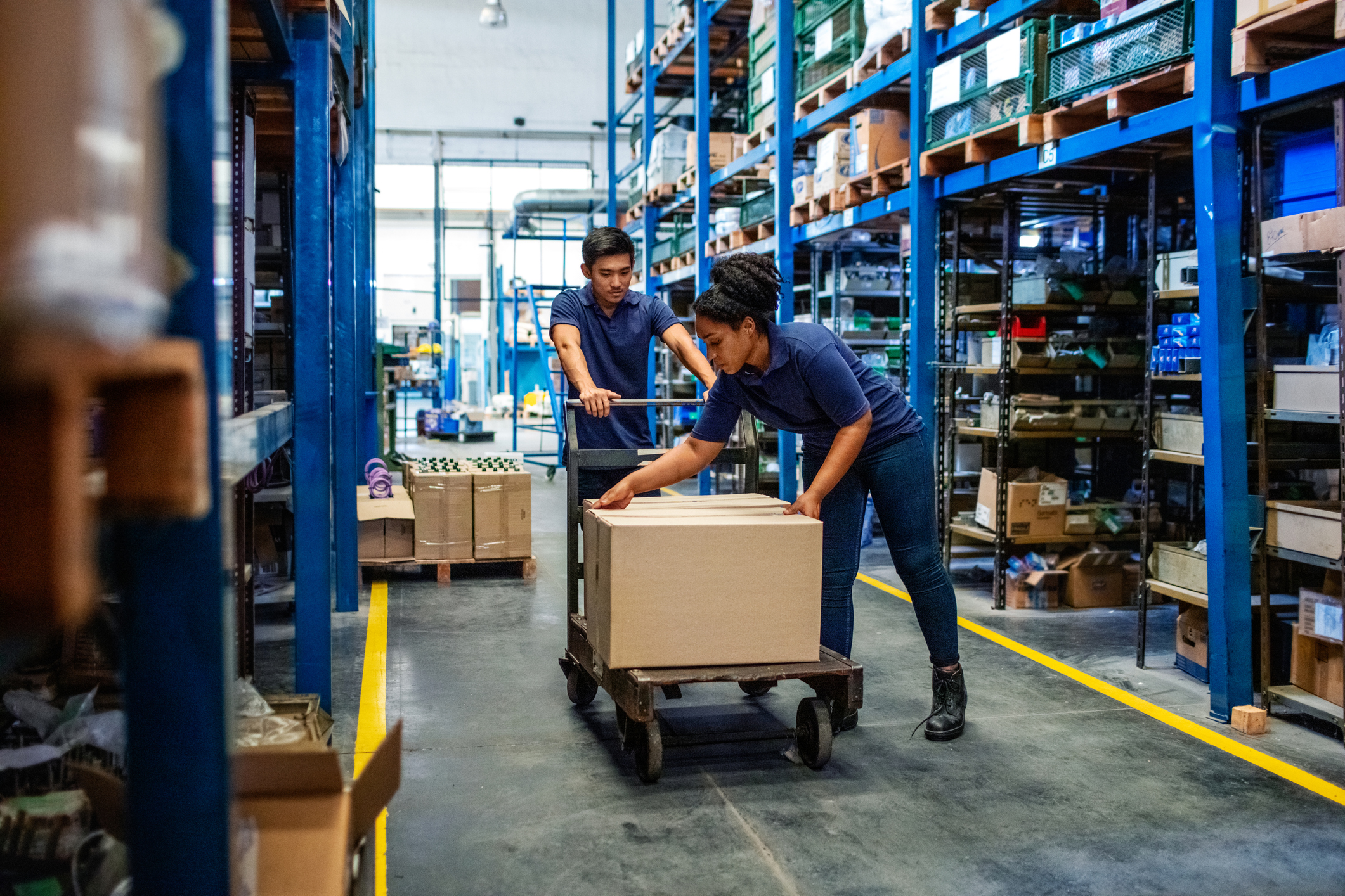 Two warehouse workers with boxes on a cart.