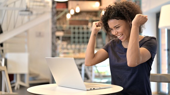 Person celebrating success on laptop in cafe. 