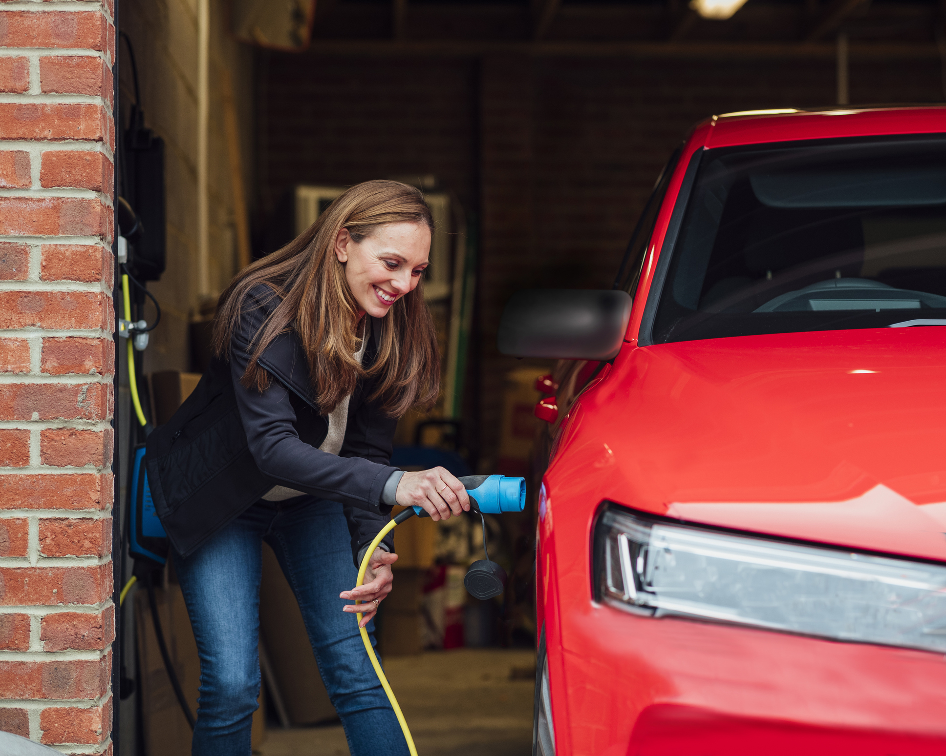 A happy person plugs in their red car to charge.