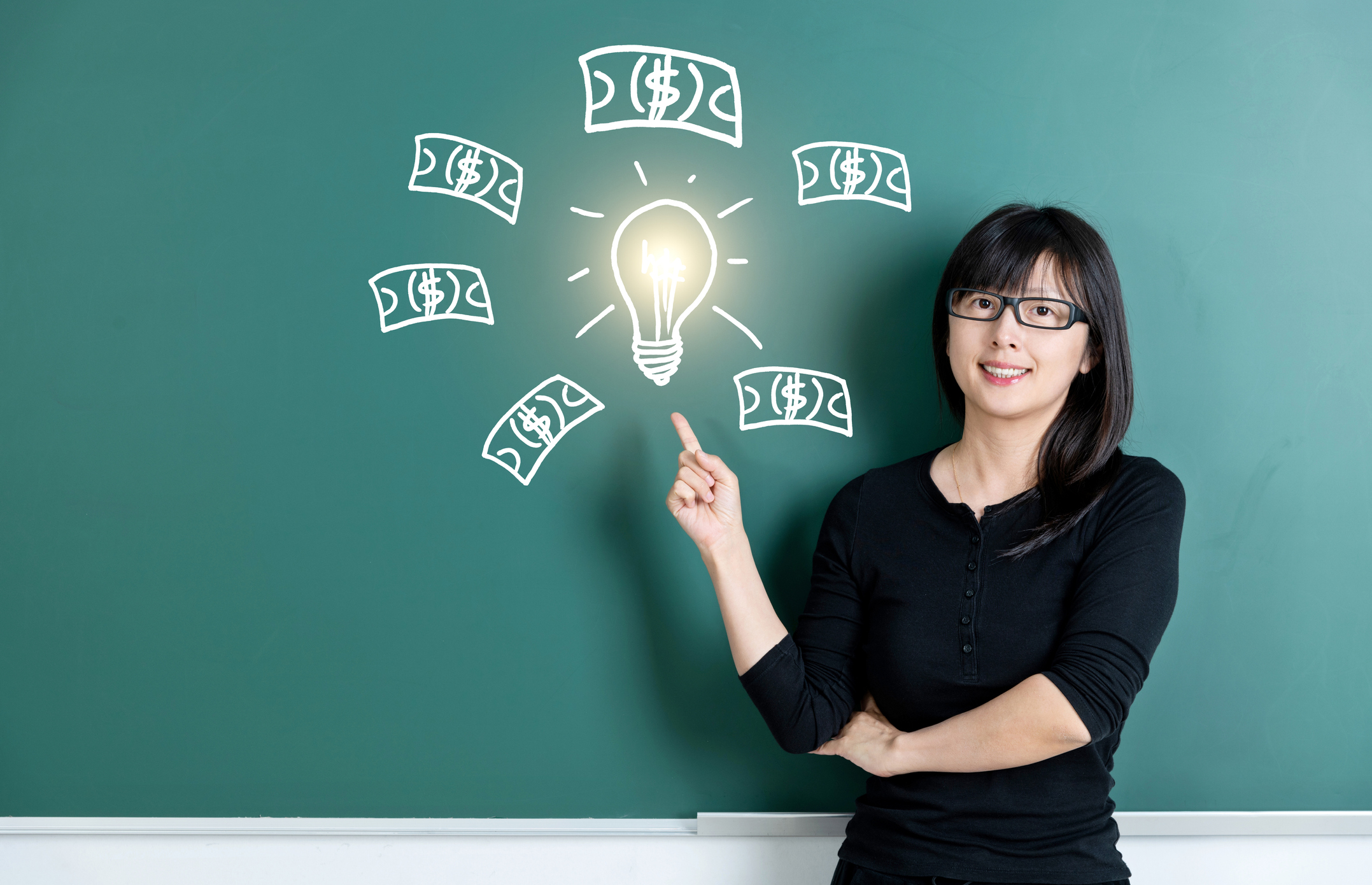 A smiling person pointing to a chalkboard drawing of a light bulb surrounded by money.