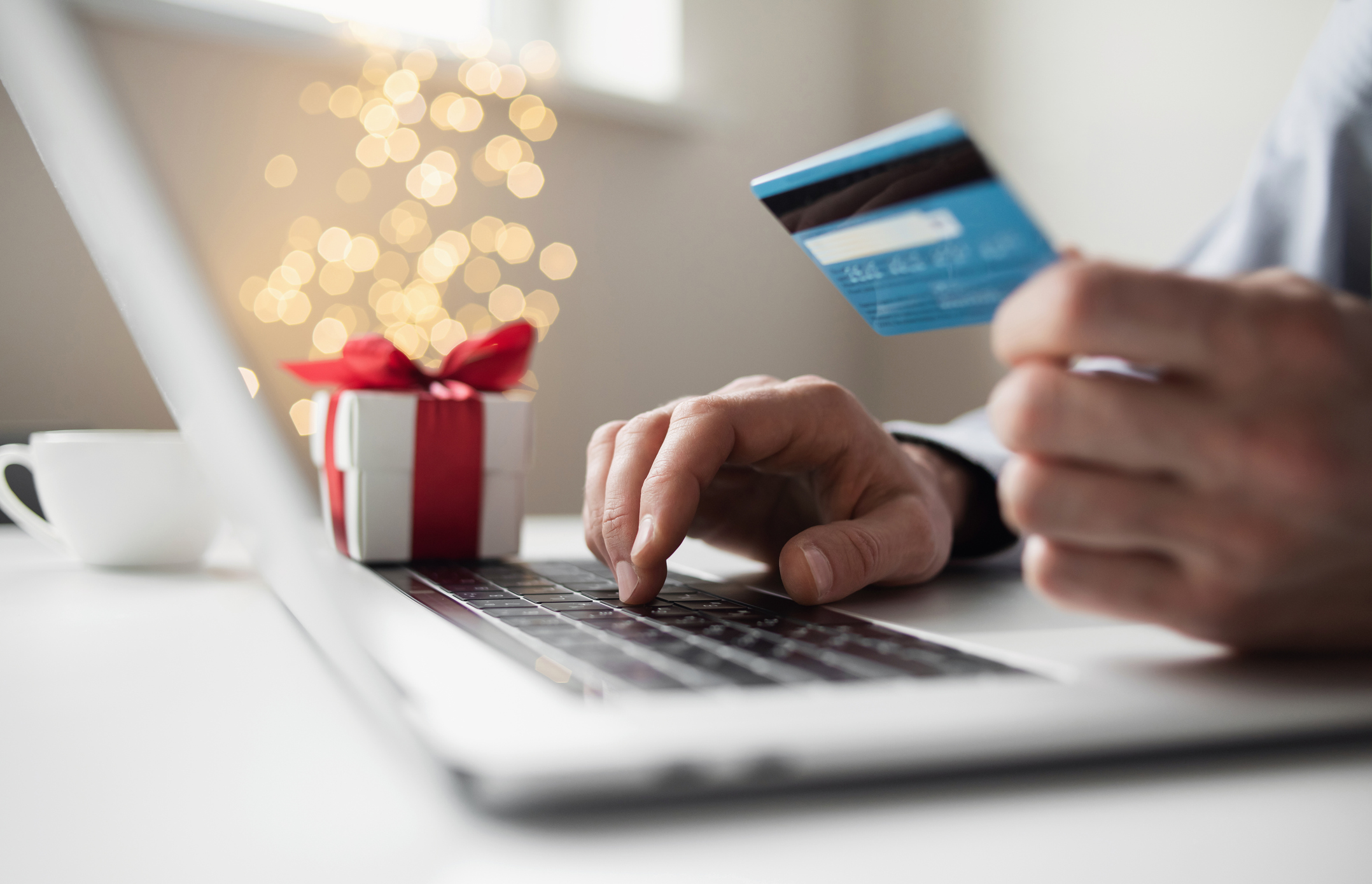 Customer holds up their credit card while doing some holiday shopping on their laptop.