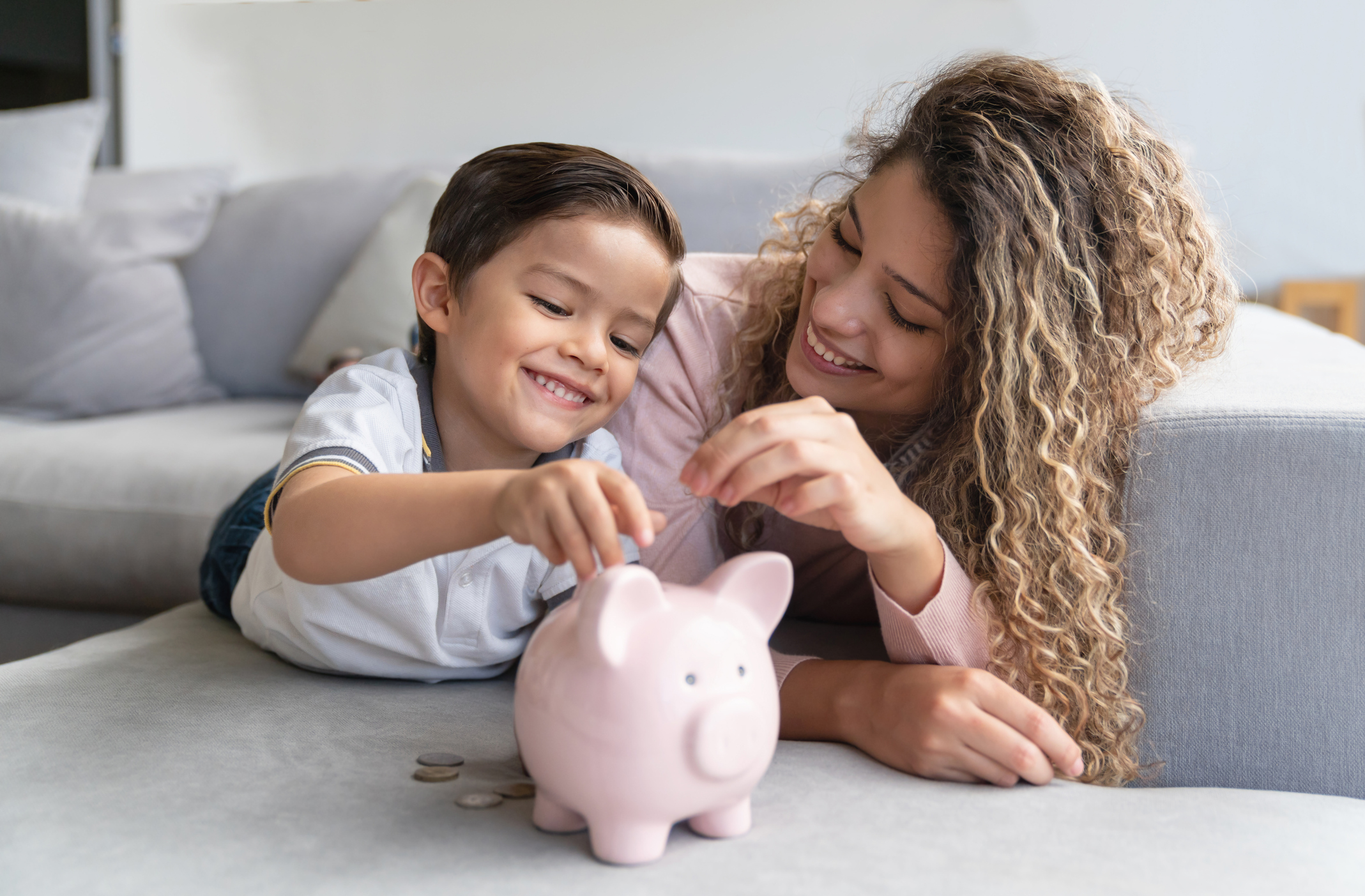 A parent helping child place coins in a piggy bank.