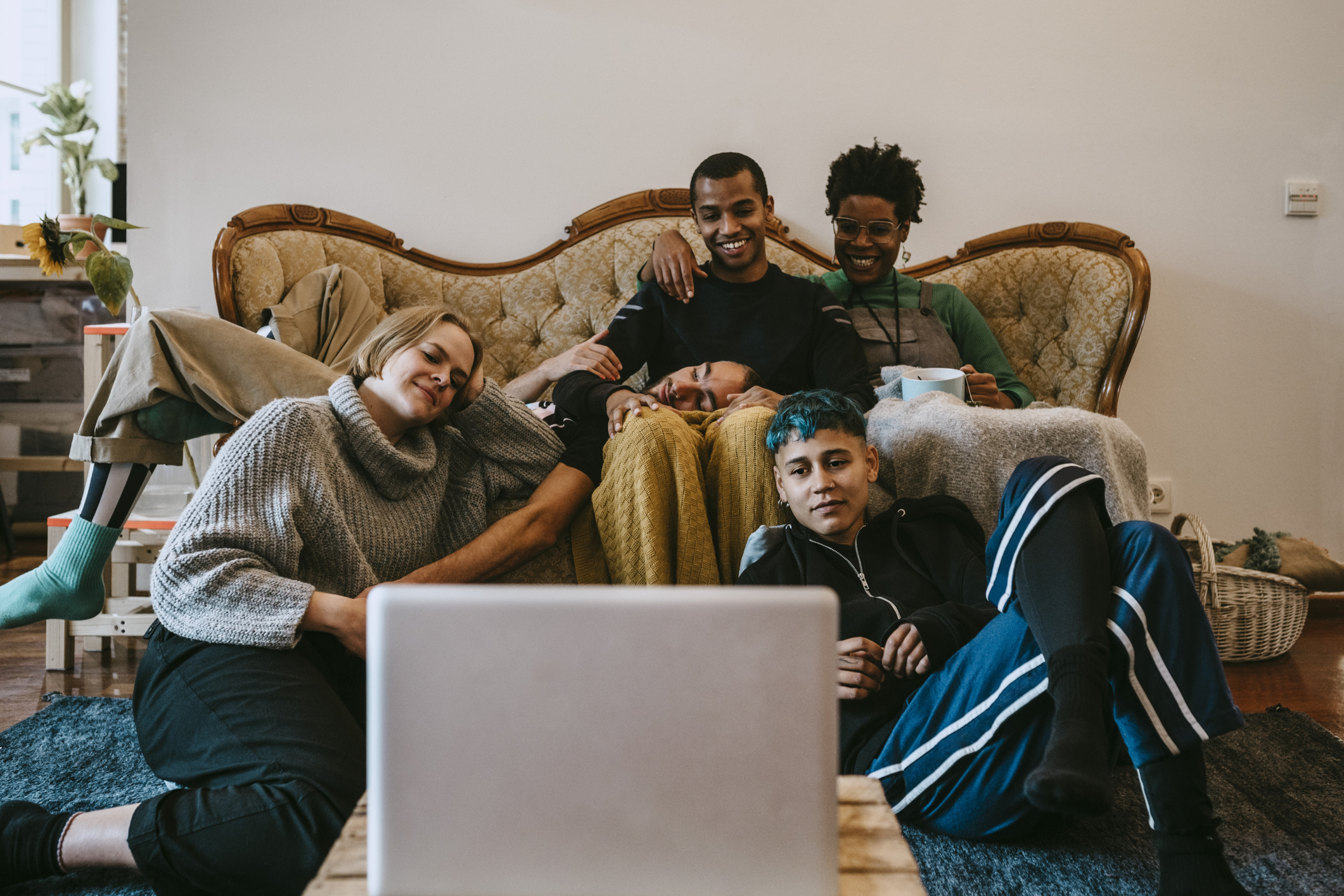 Five young adults sitting lounging about a living room watching streaming on a laptop.