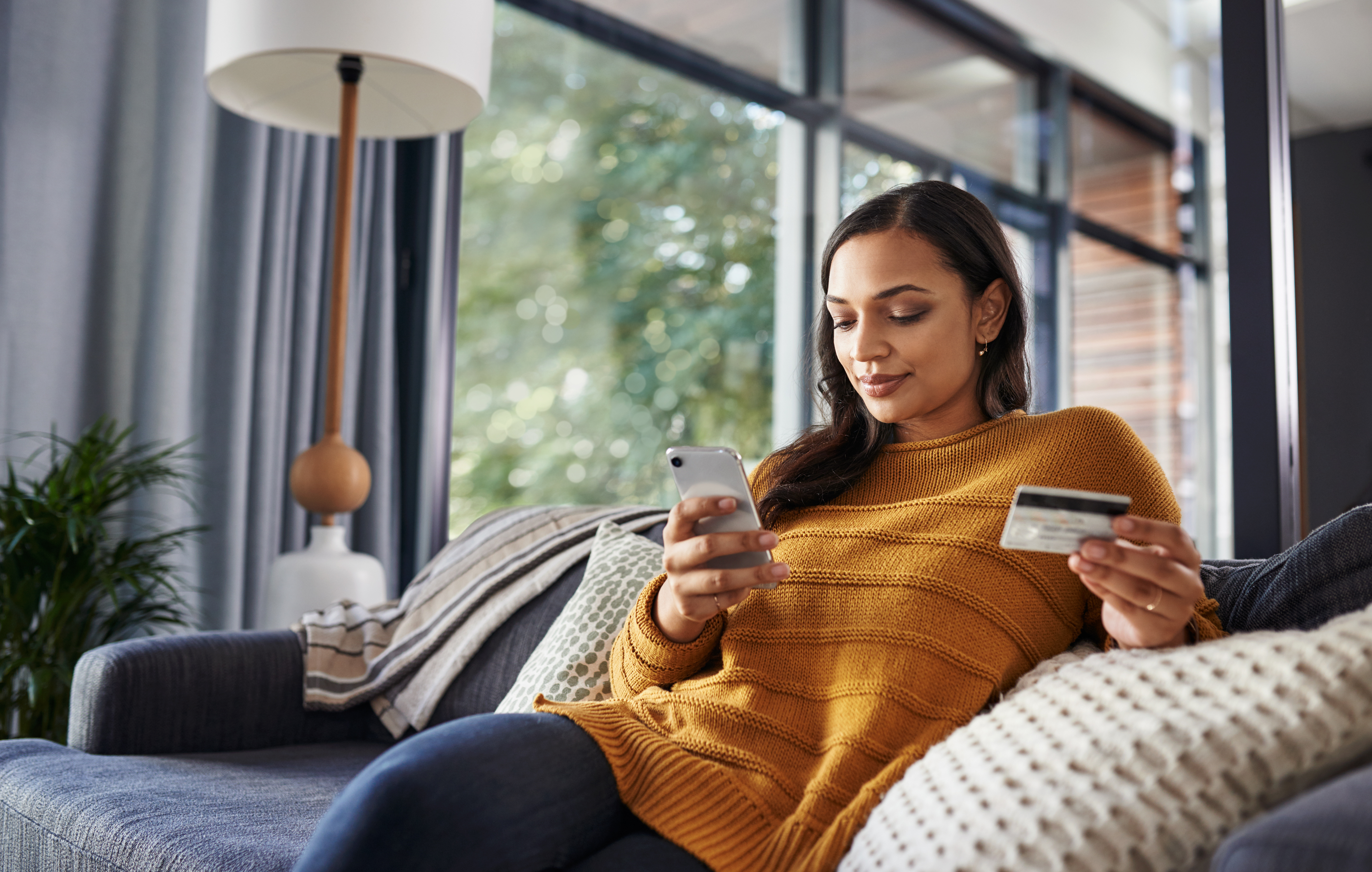 A young person sitting on the couch online shopping with credit card in hand.