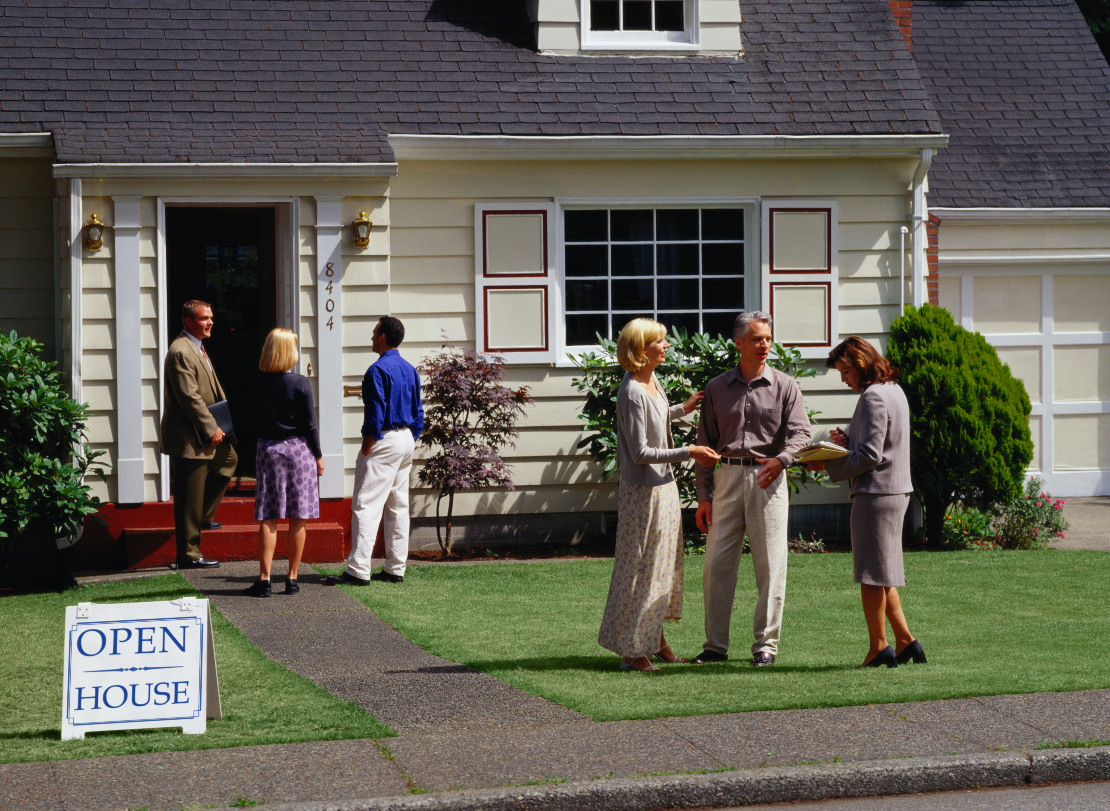 People standing outside of house with open house sign in front of it.