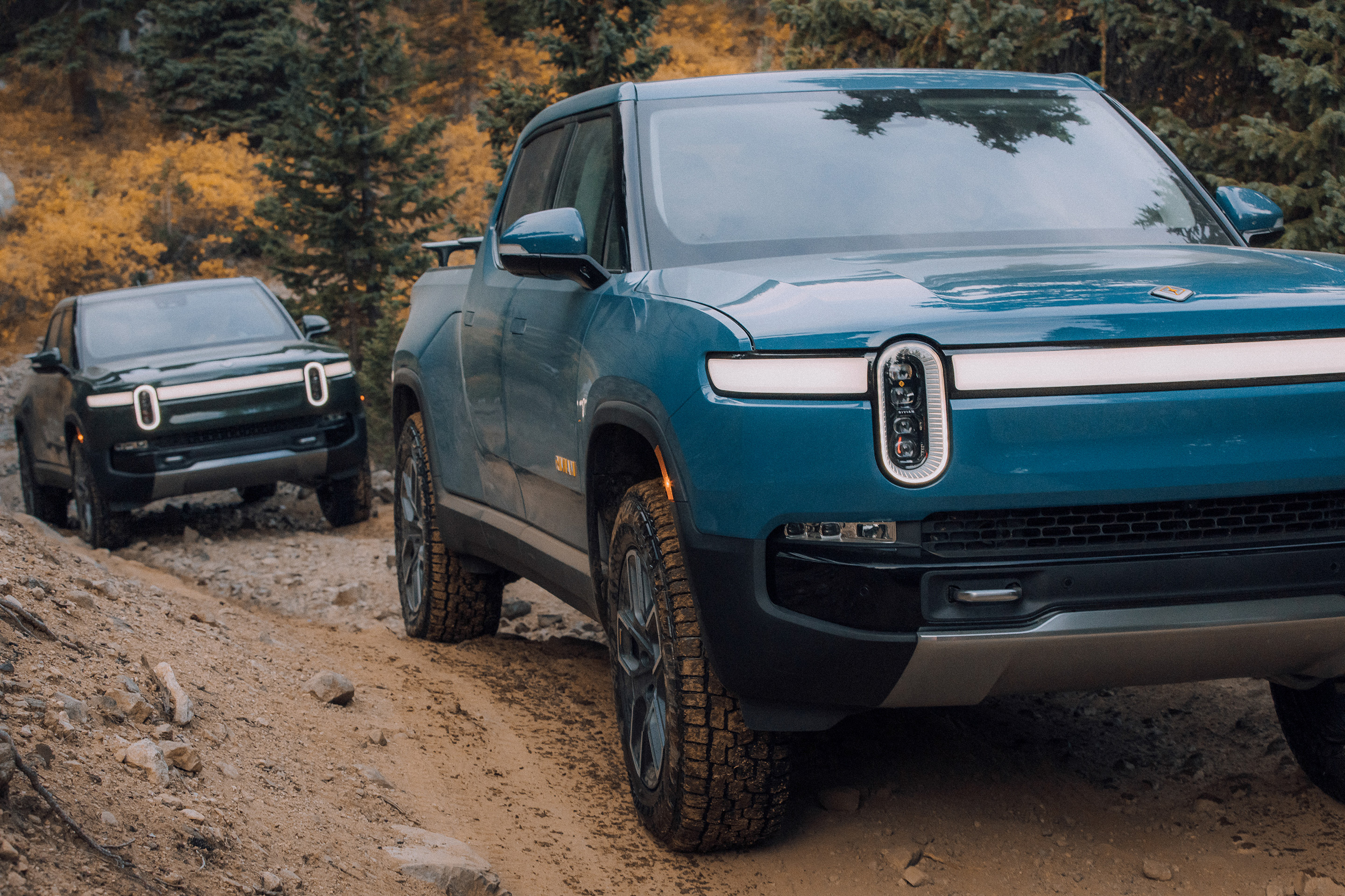 Two Rivian R1T's climbing a muddy road.