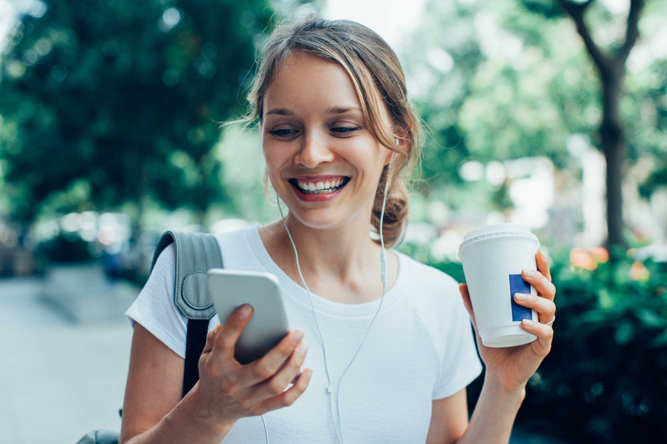 Smiling person with cup looking at mobile phone.