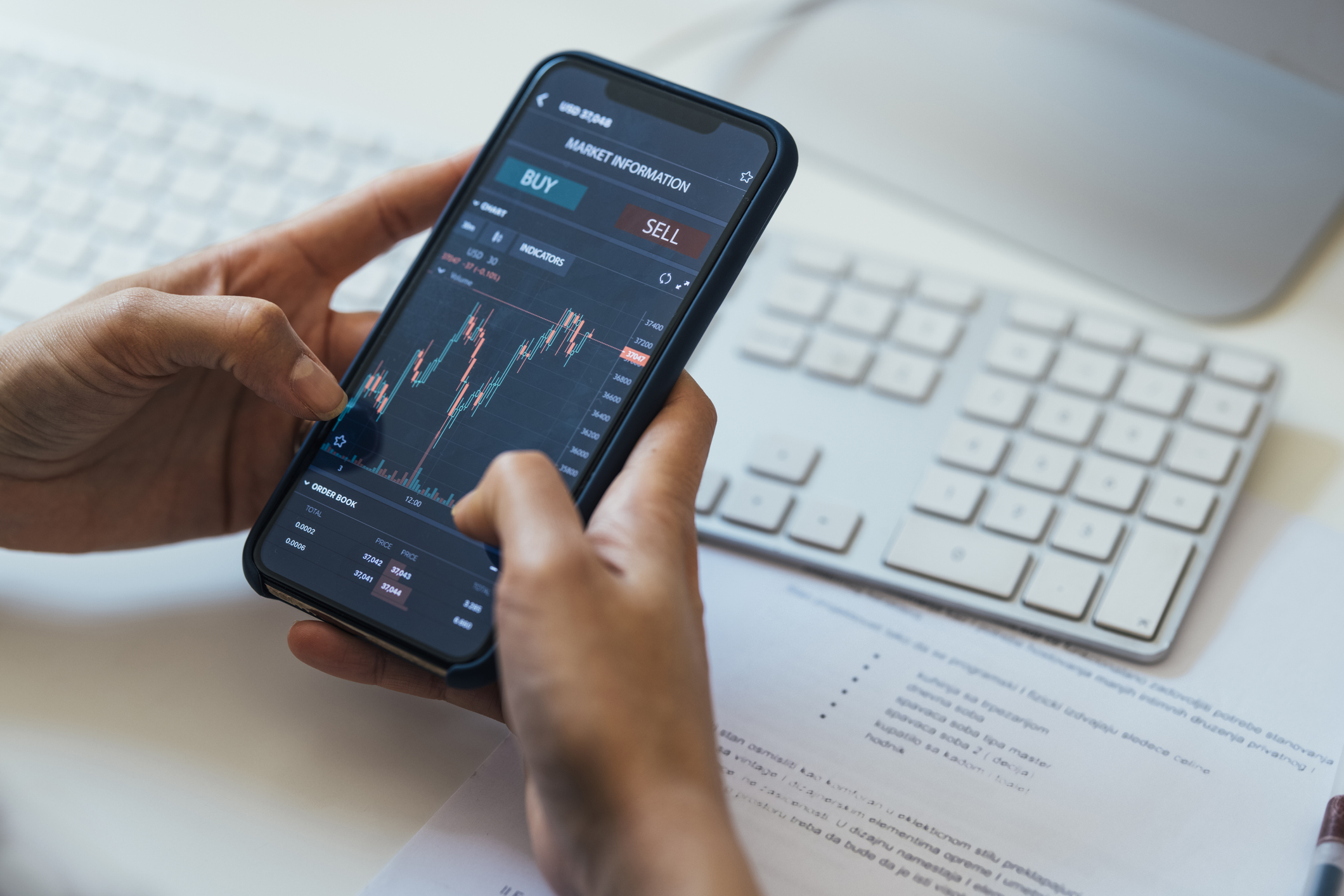 A person holding a smartphone displaying a volatile crypto chart with buy and sell buttons above it.