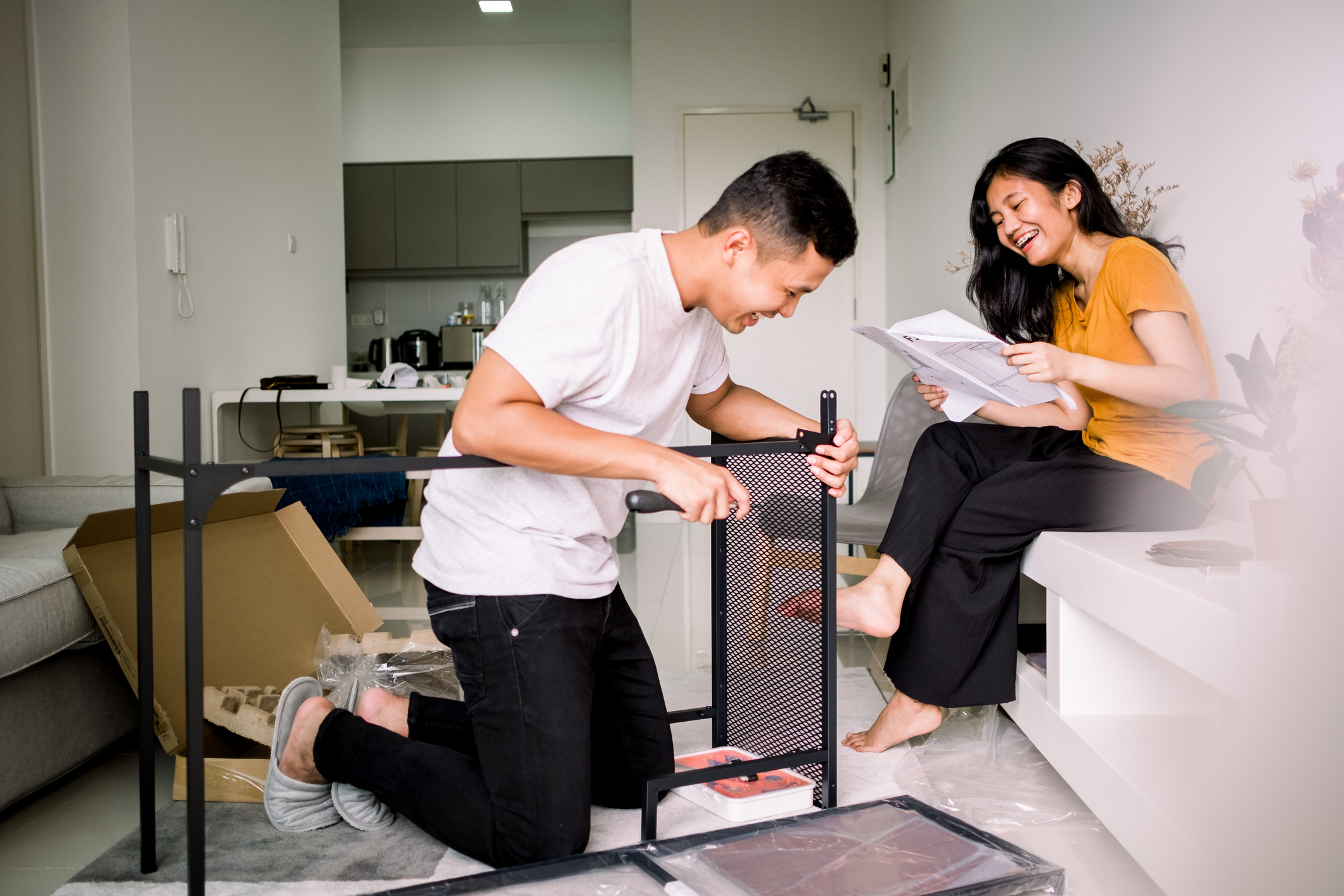 Two people smile while assembling furniture in a new apartment.