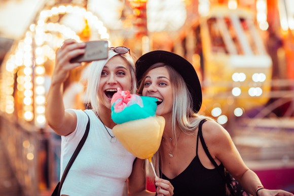 Two people taking a selfie while holding cotton candy at an amusement park.