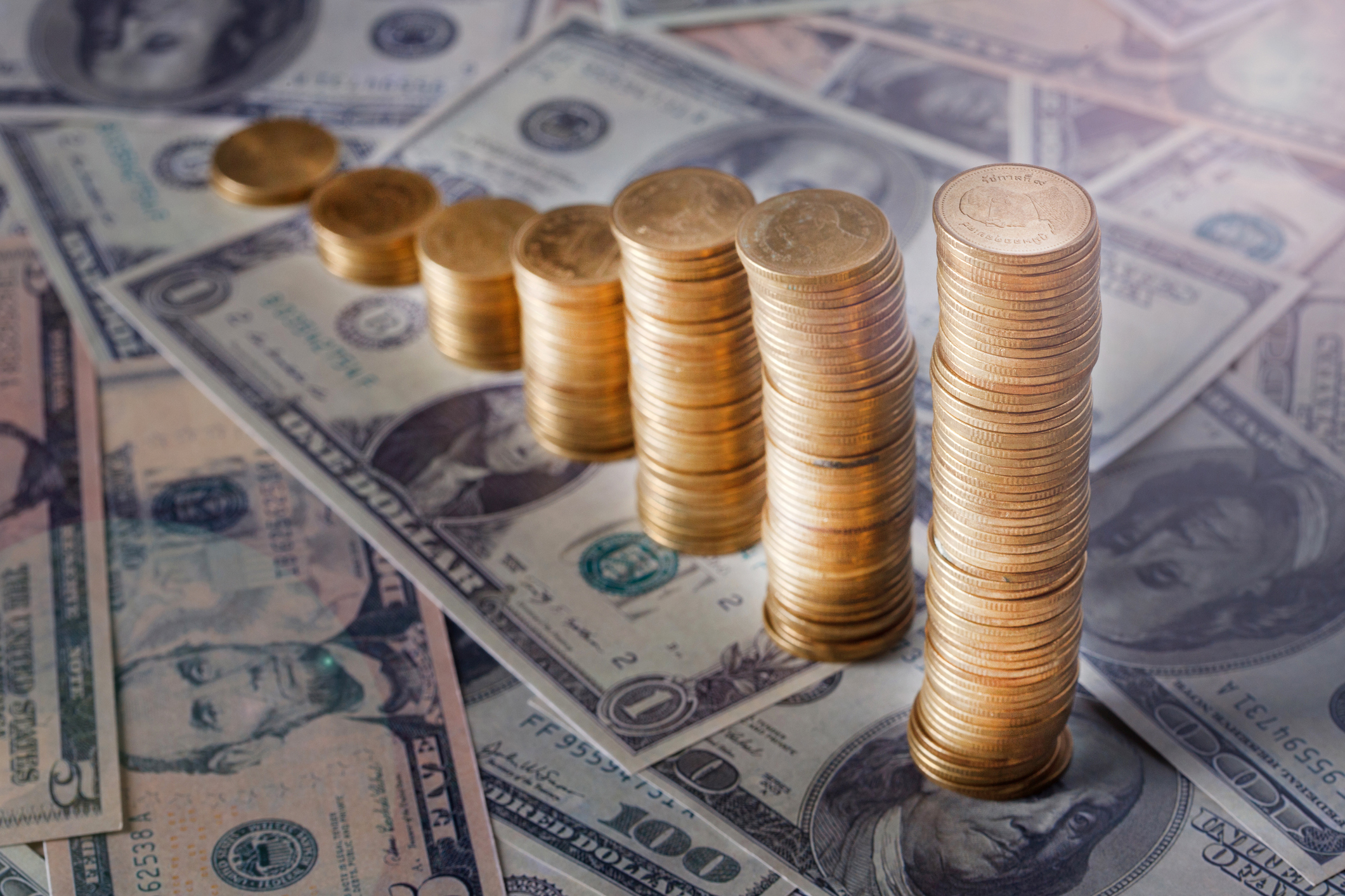 Stacks of gold coins on top of dollar bills.