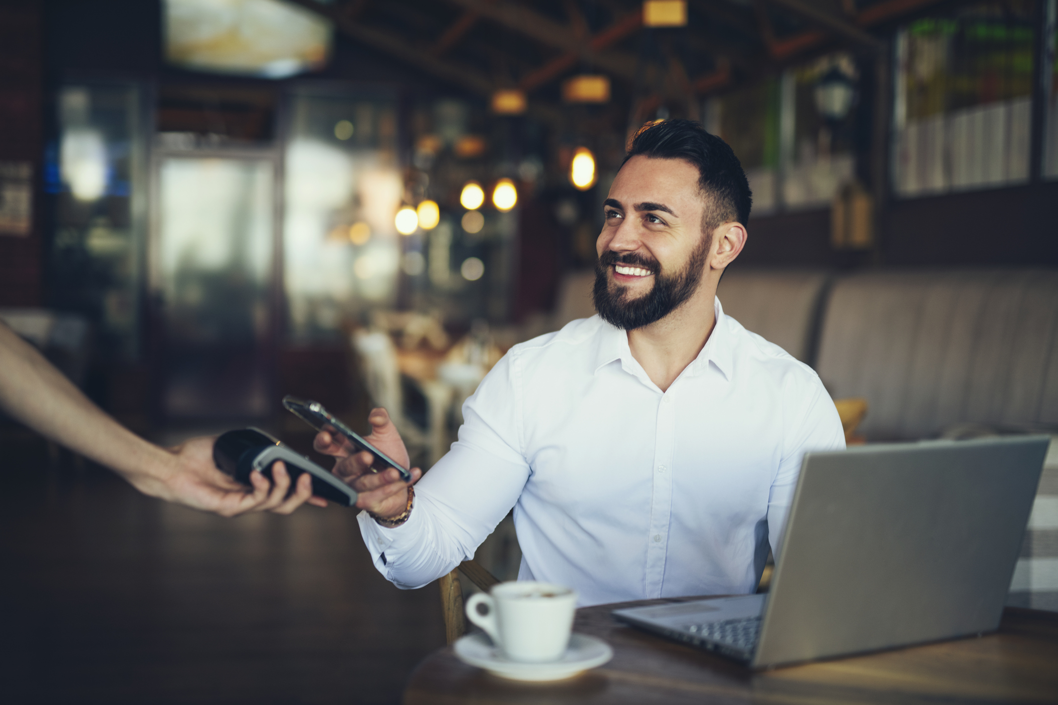 A smiling person in a restaurant making a digital payment with a smartphone.