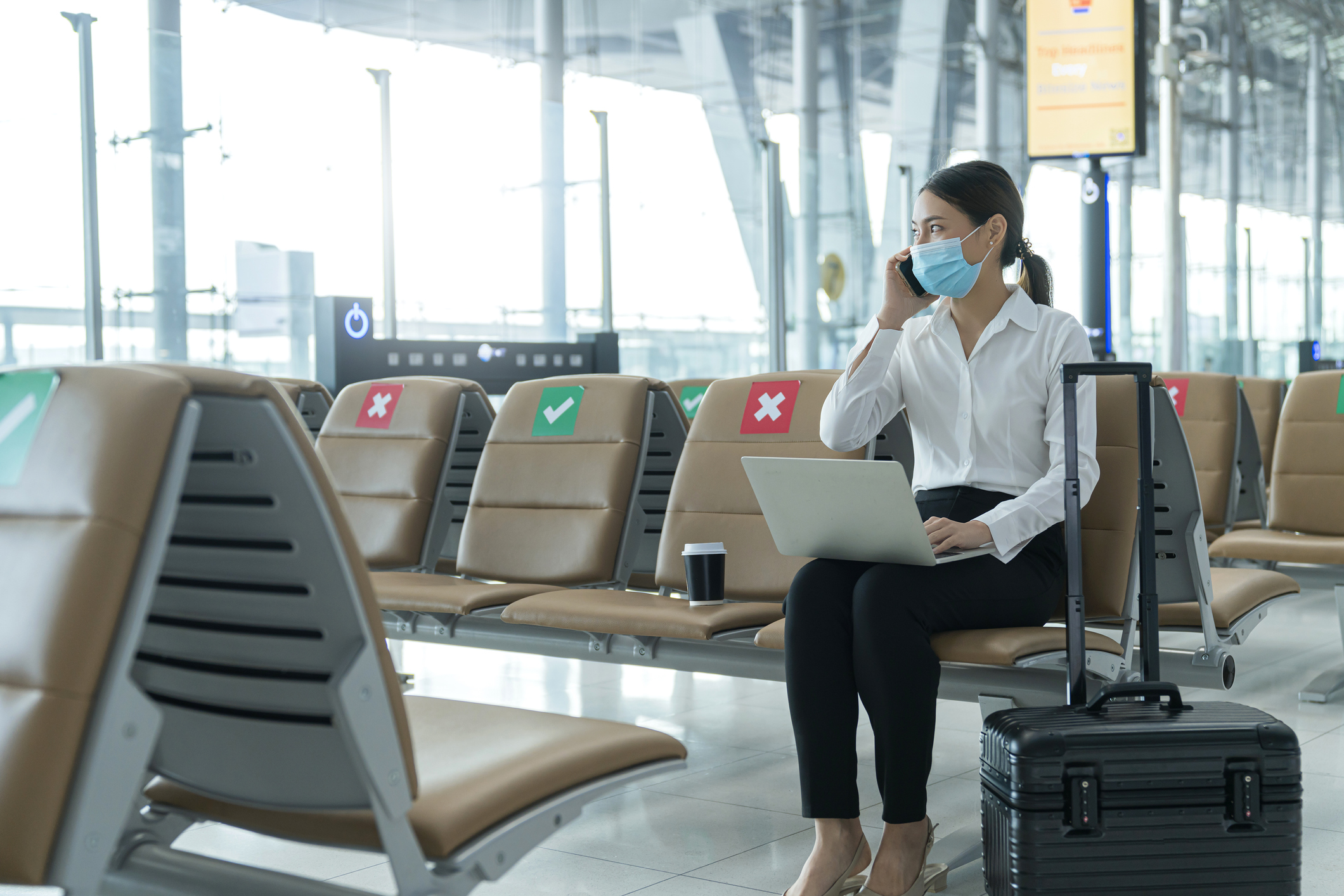 A businessperson travels in an airport with luggage and laptop.