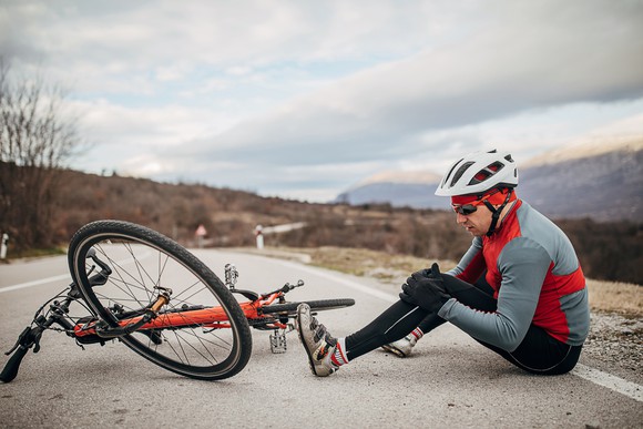 Cyclist nurses a hurt knee while sitting next to a fallen bicycle.