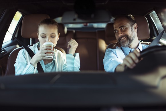 Two people in a car, one drinking coffee.
