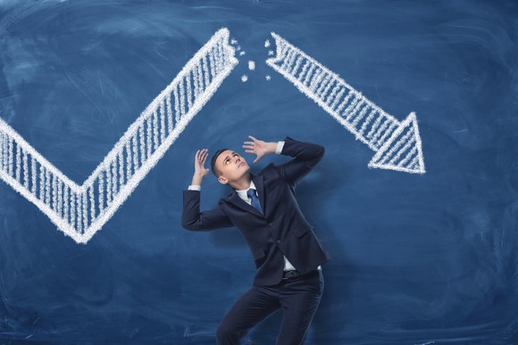Scared person standing next to a stock chart that's pointing downward.