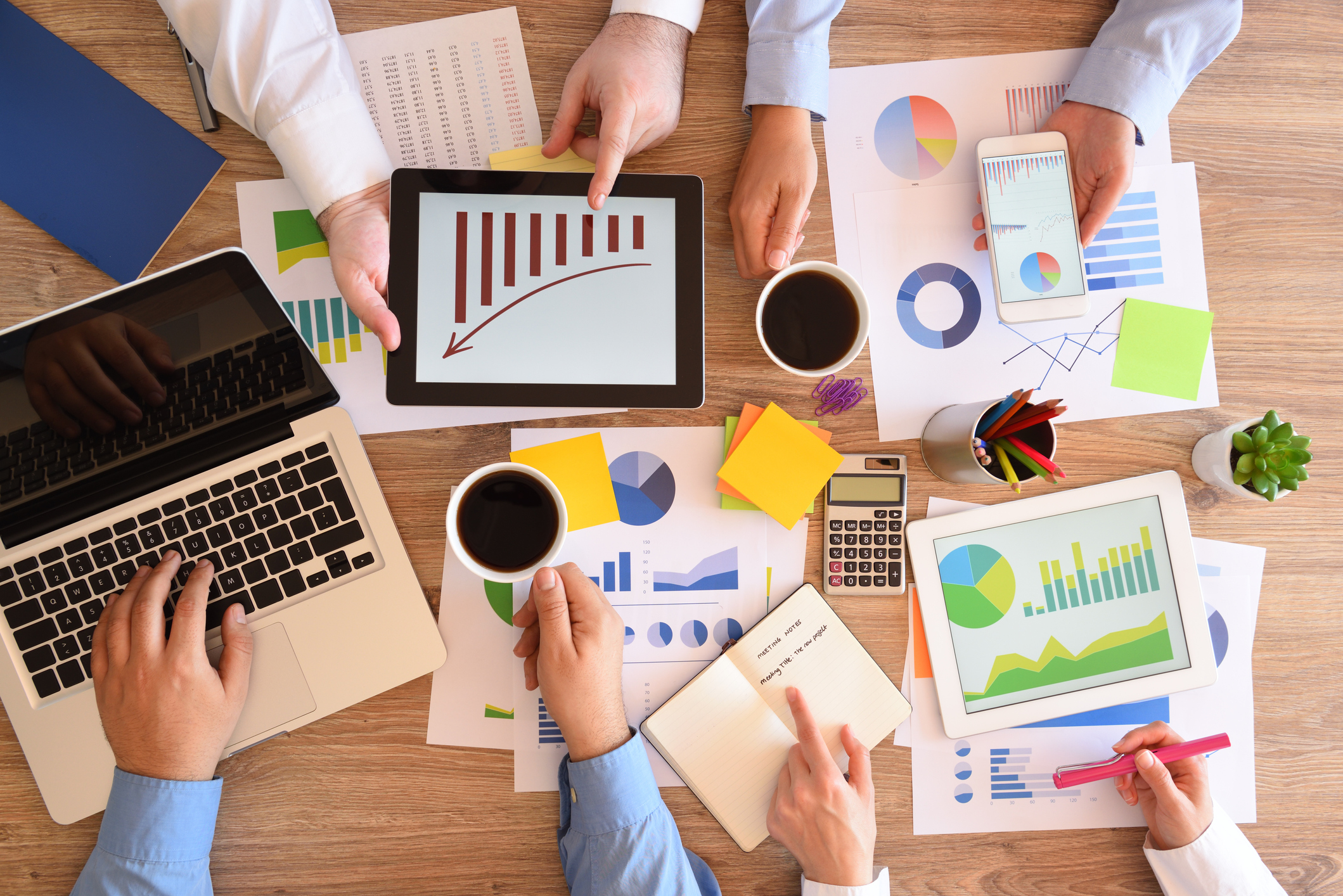 Investors examining charts on paper, digital tablets, and computers.