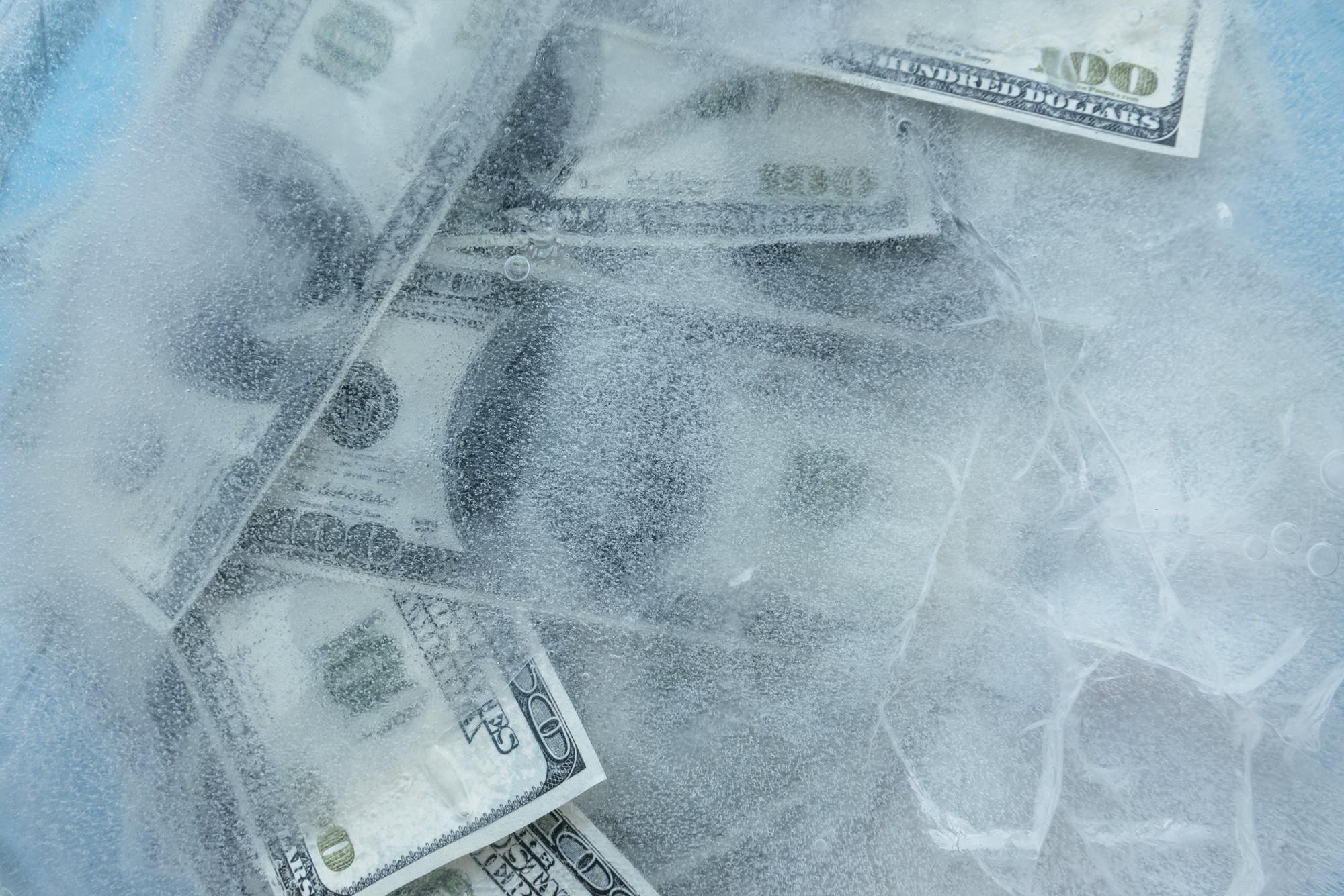 Several U.S. $100 bills lie frozen under a sheet of ice.