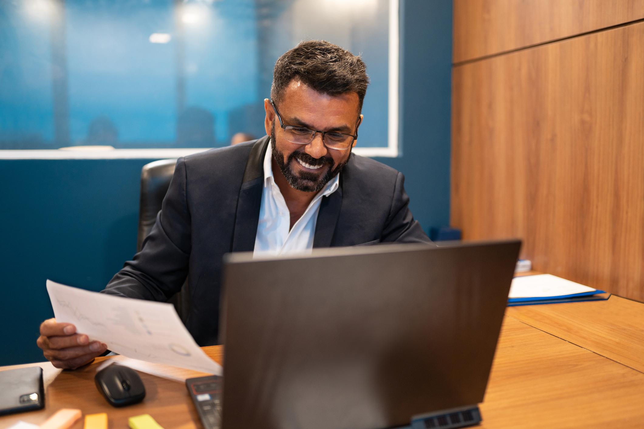Businessman reviewing a paper document while looking at his computer.