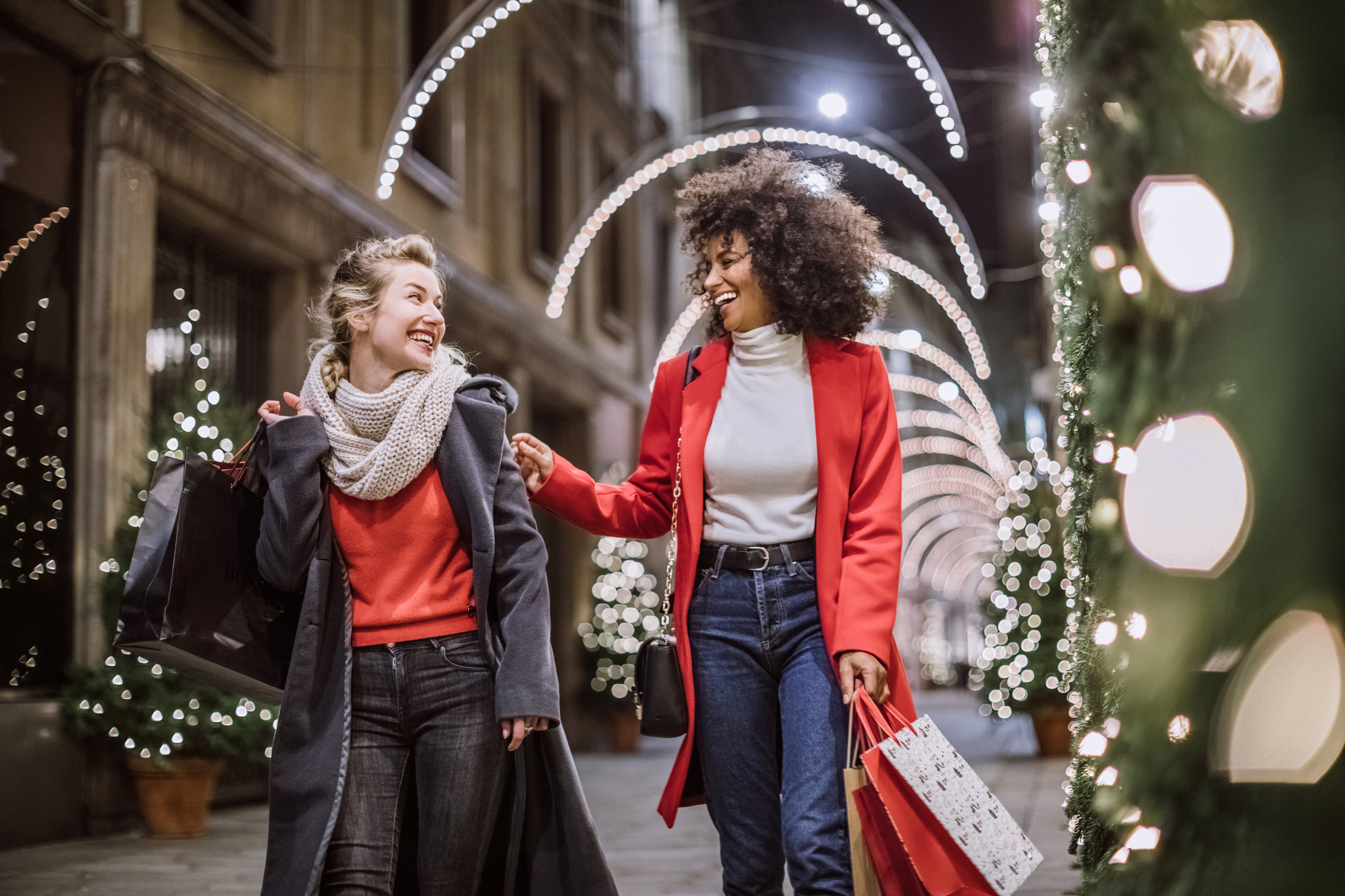 Two ladies dressed in red walking through a shopping center with a handful of bags.
