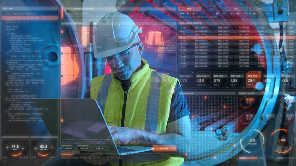 A person wearing a hard hat working on a laptop.