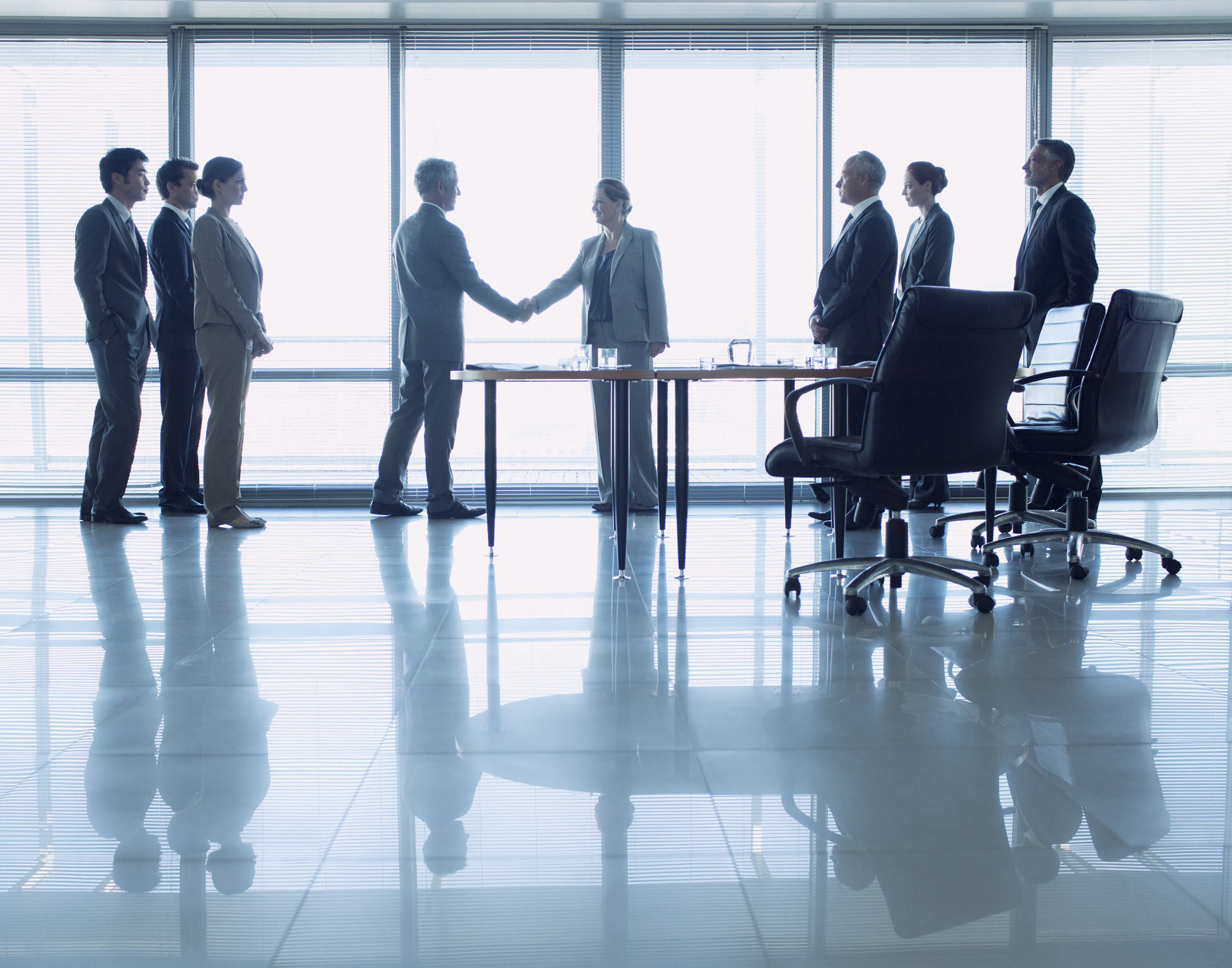 A group of people inside a conference room with two people shaking hands.