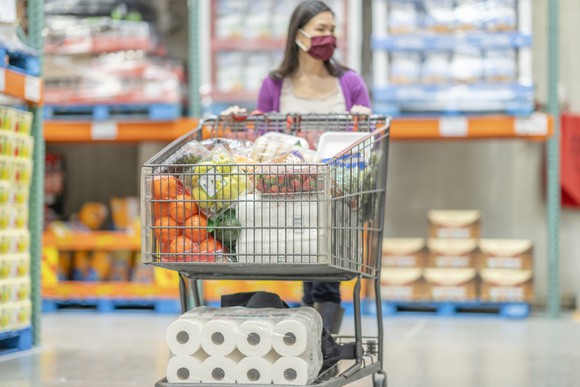 A masked shopper pushes a full cart through a grocery store.