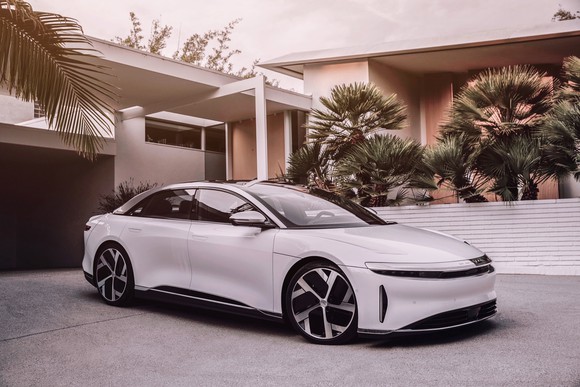 A white Lucid Air sedan parked in-front of a modern home. 