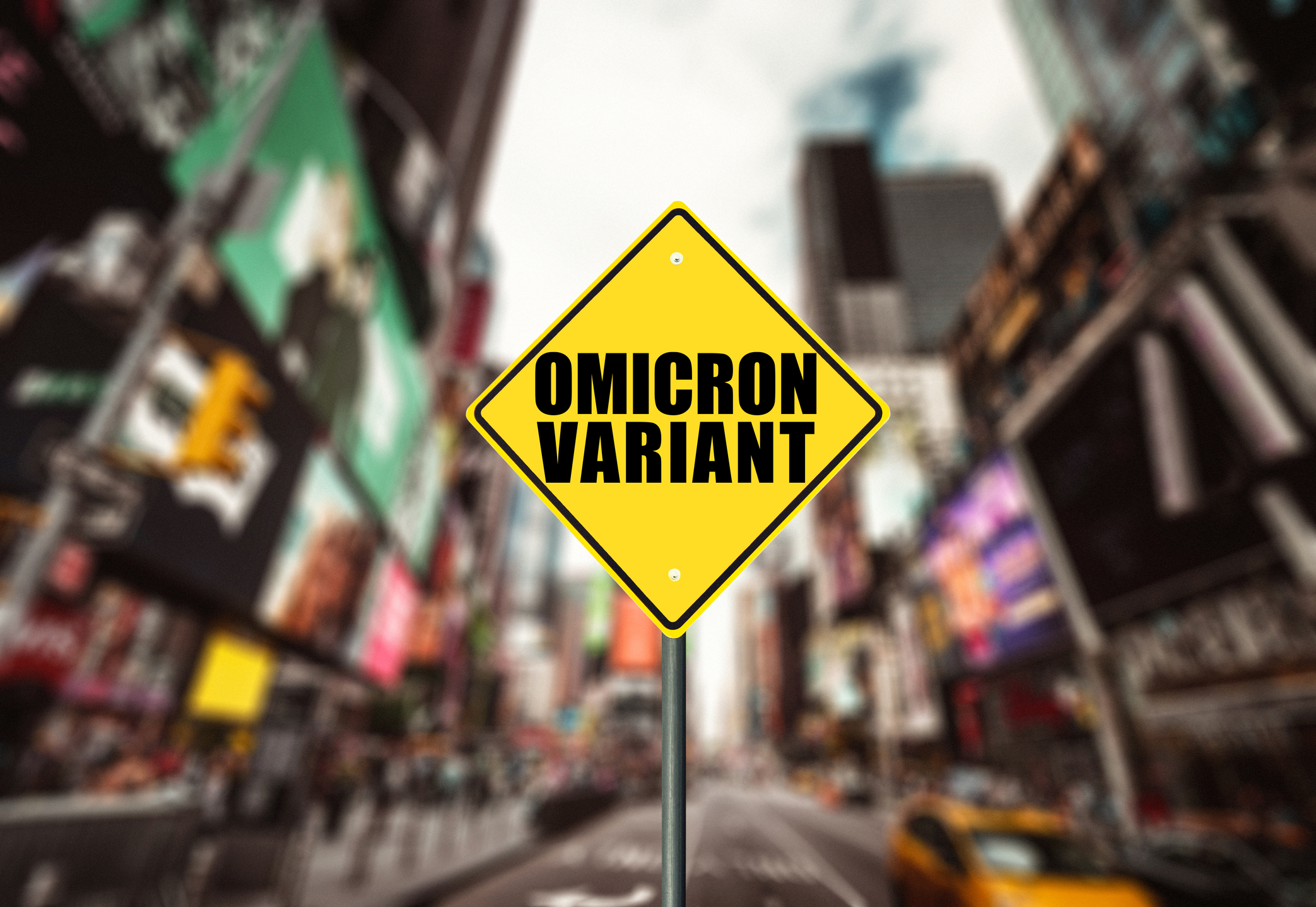 Street sign reading "Omicron Variant" with a blurred city street in the background.
