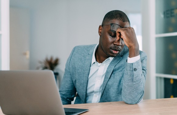 A businessman holds his head while sitting in front of a laptop.