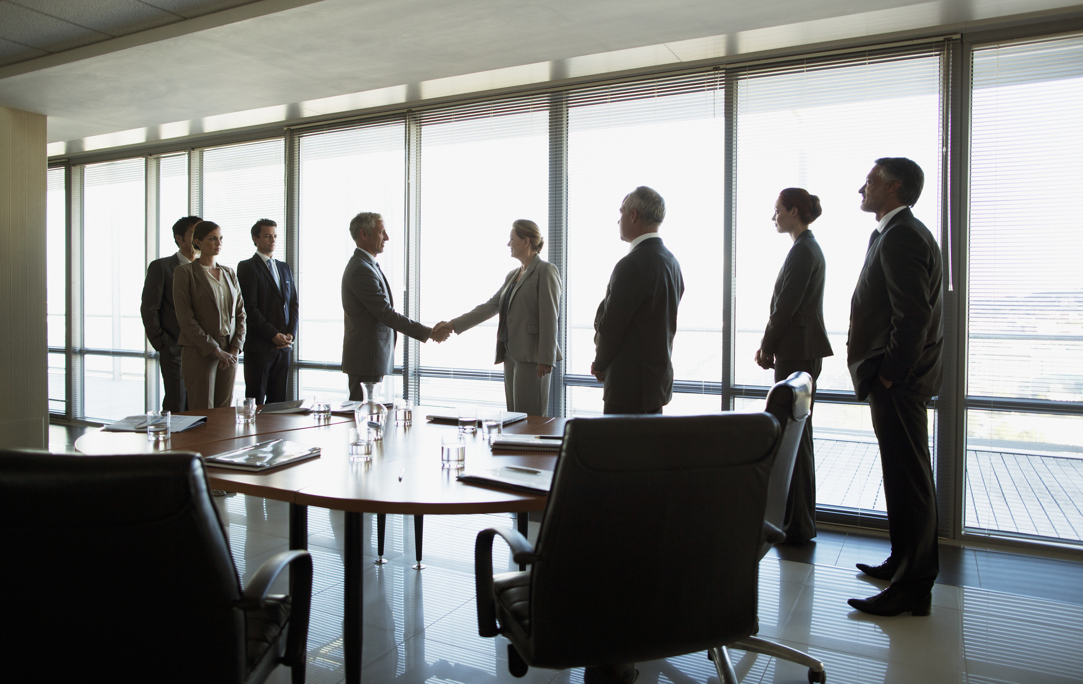 Executives in a boardroom with two shaking hands.