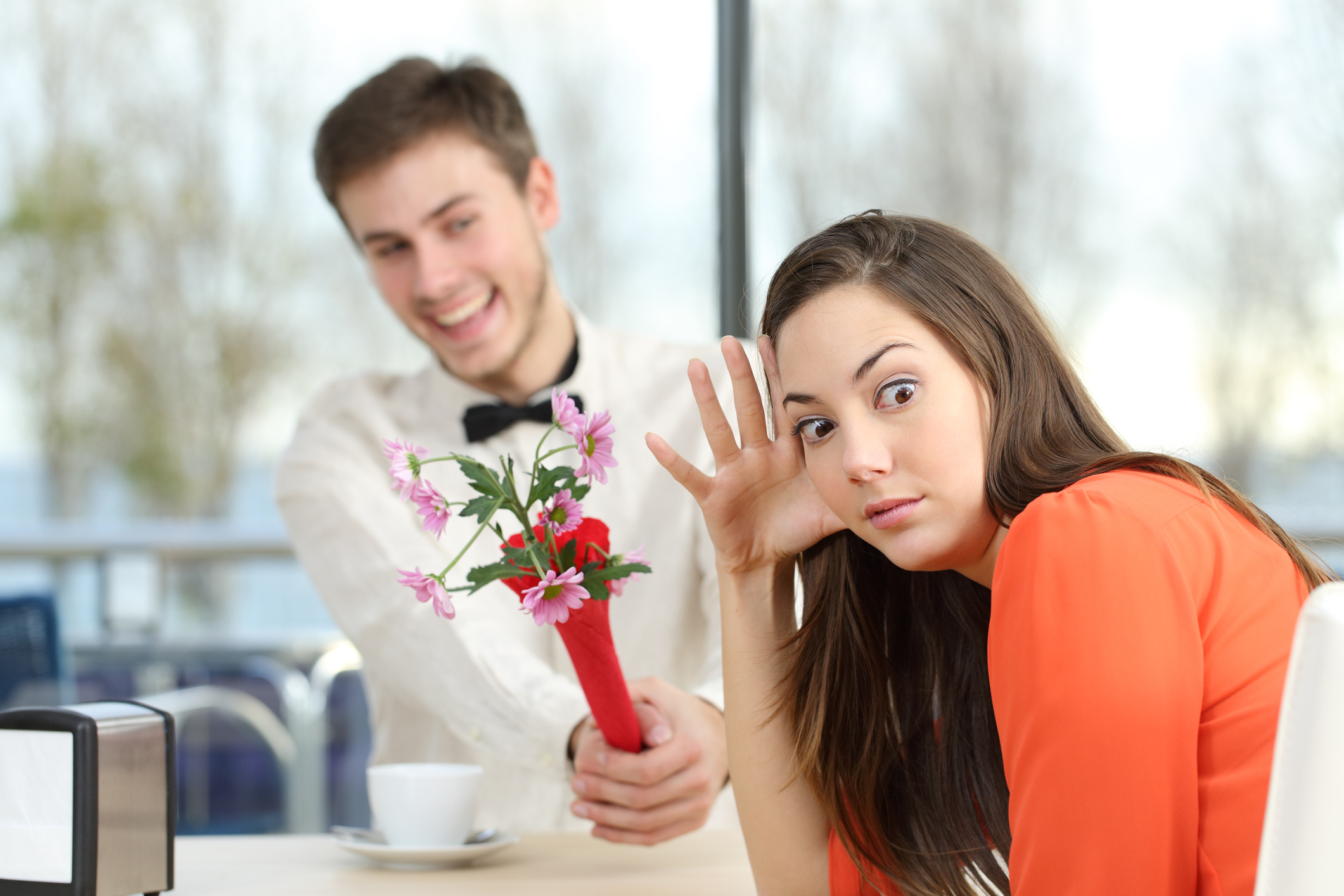A person tries to hide from a blind date carrying a bouquet.