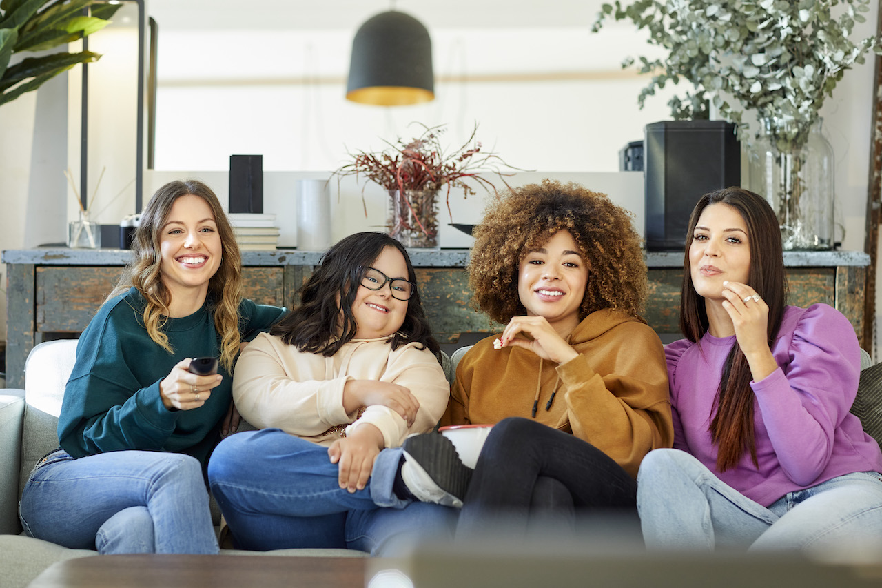 A group of friends watch TV together on a couch.
